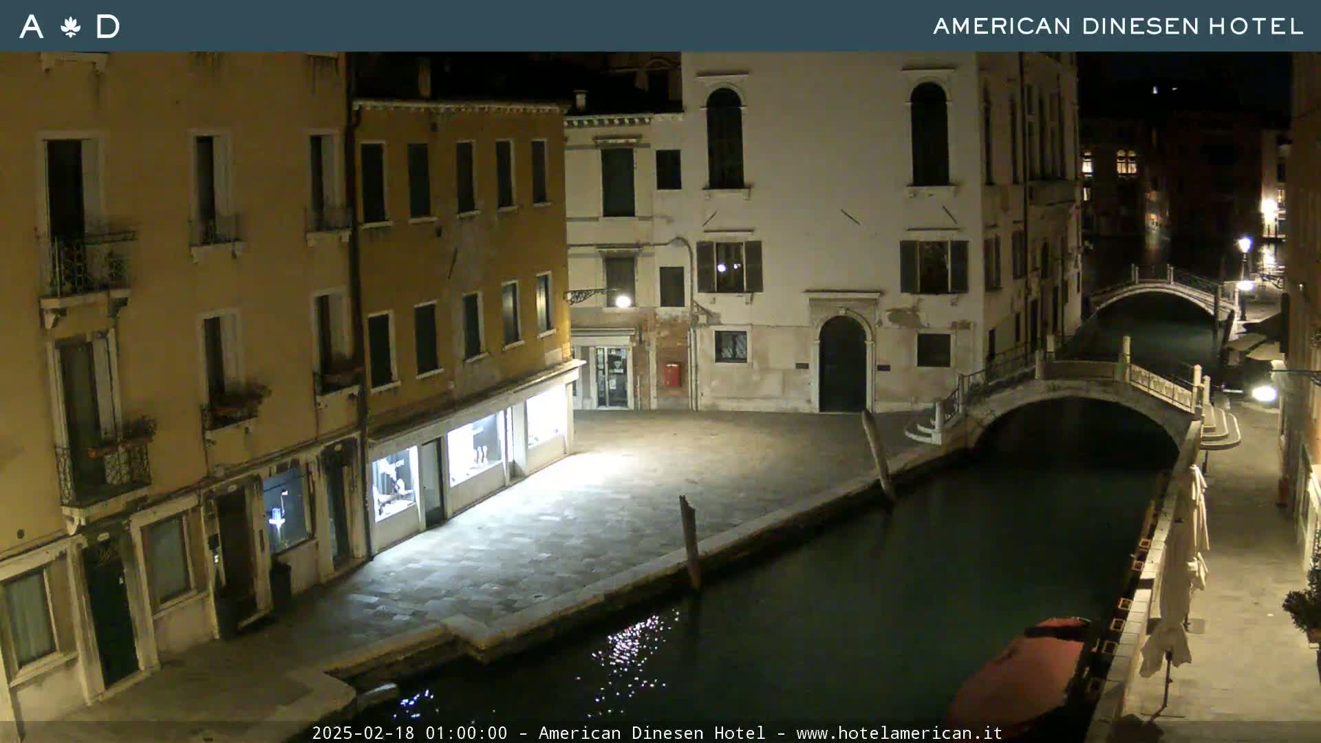 A nighttime view of a canal in Venice, Italy, shows several buildings lining the waterway and a small bridge spanning the canal.