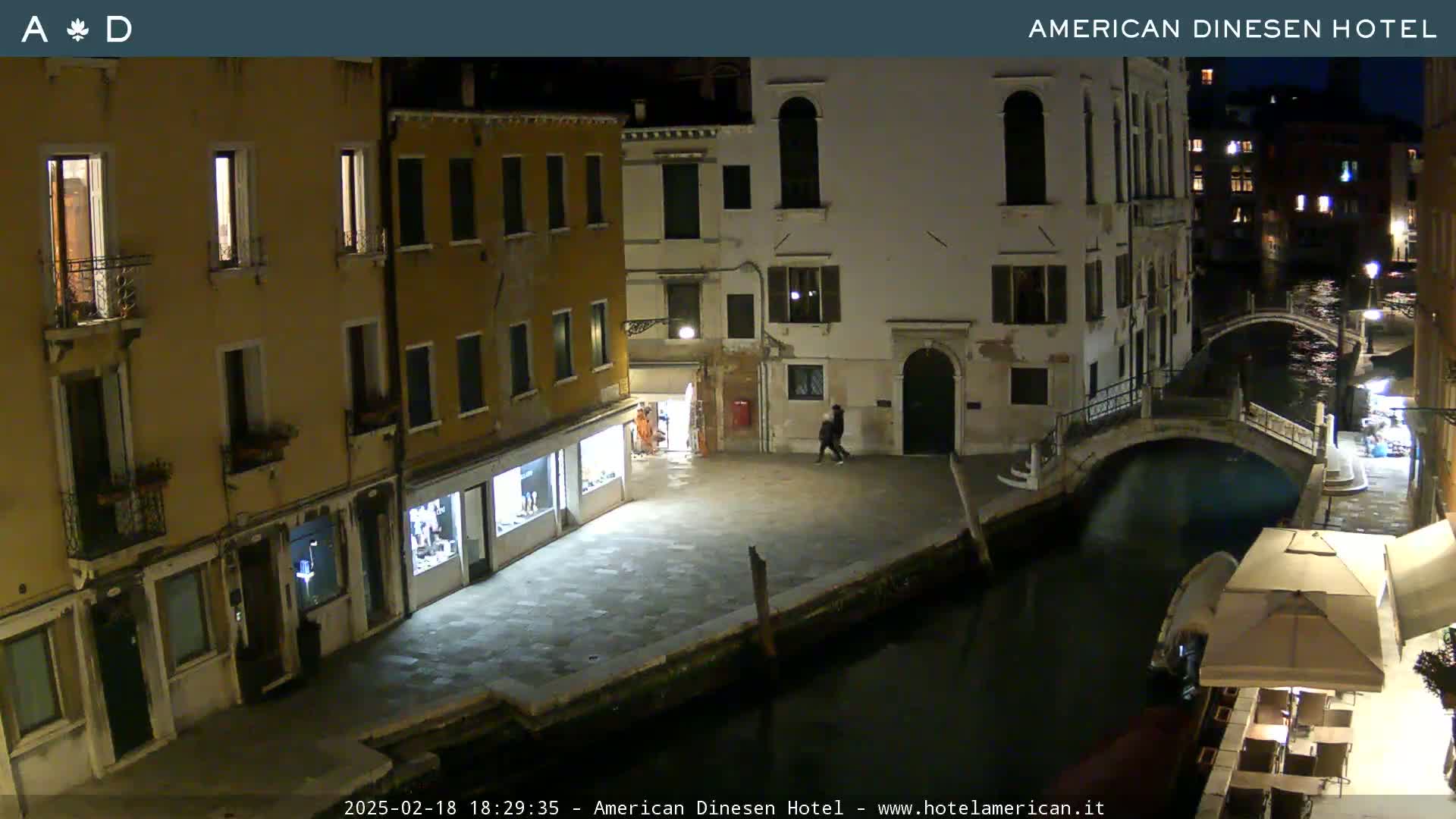 A nighttime view of a canal in Venice, with buildings lining the waterway and a small bridge spanning the canal.