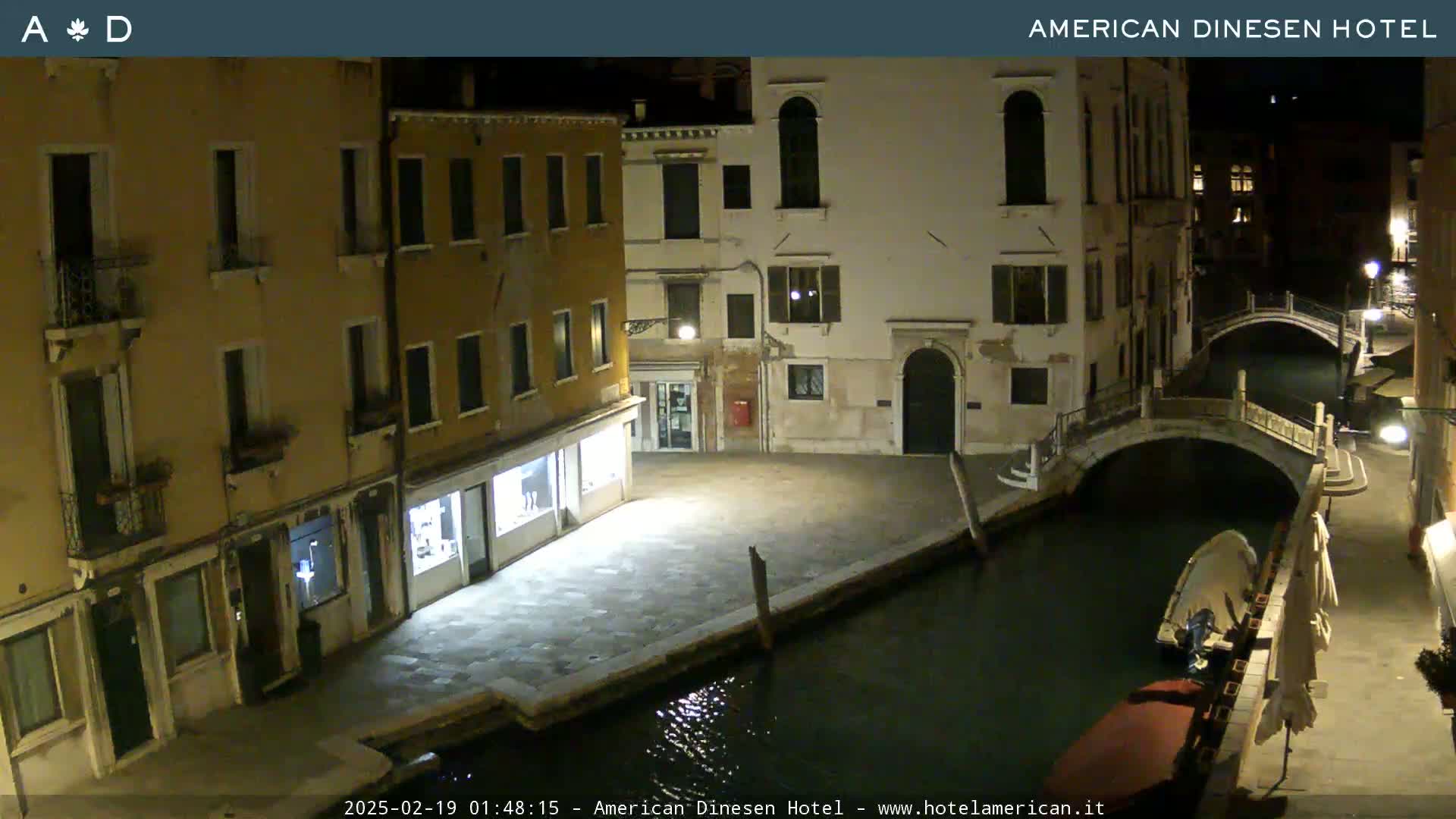 A nighttime view of a canal in Venice, with buildings lining the waterway and a small boat moored near a bridge.