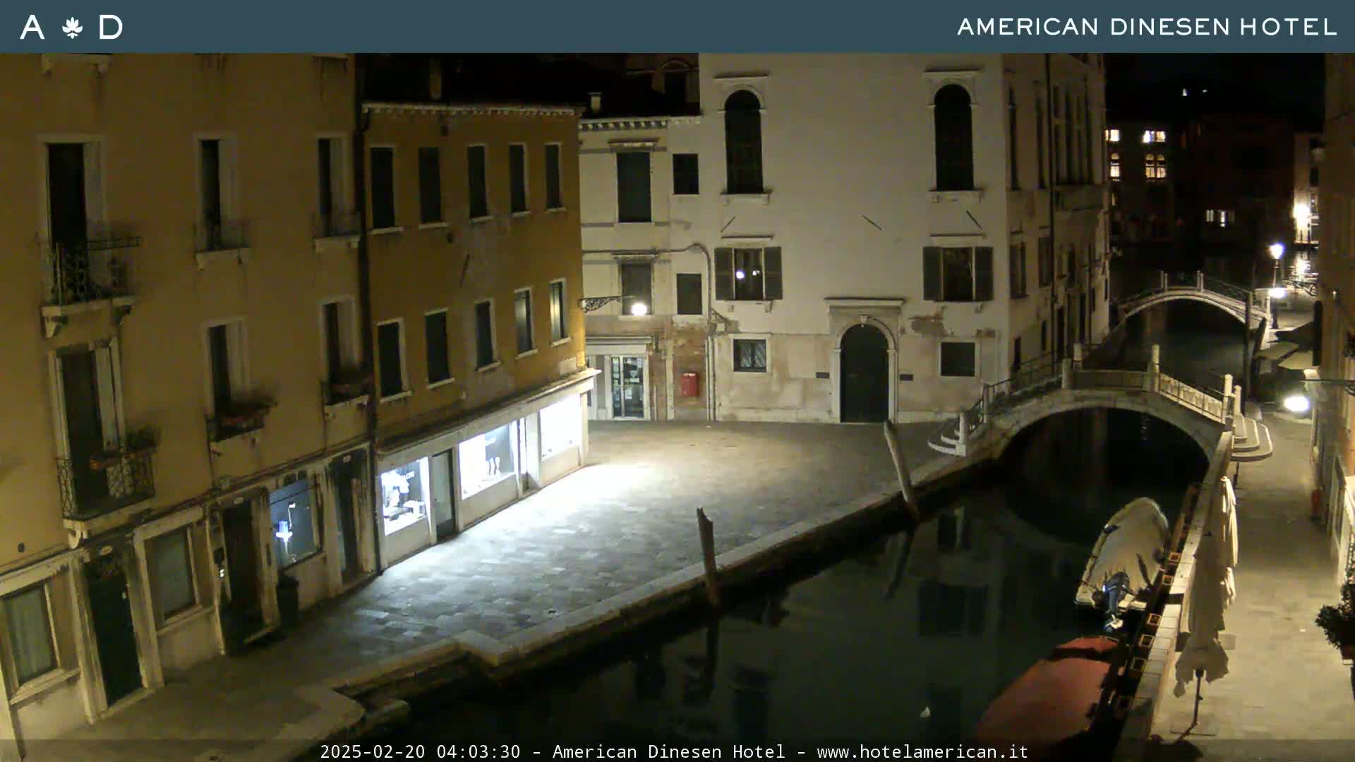 A nighttime view of a canal in Venice, showing several buildings lining the waterway and a small boat moored alongside a stone embankment.