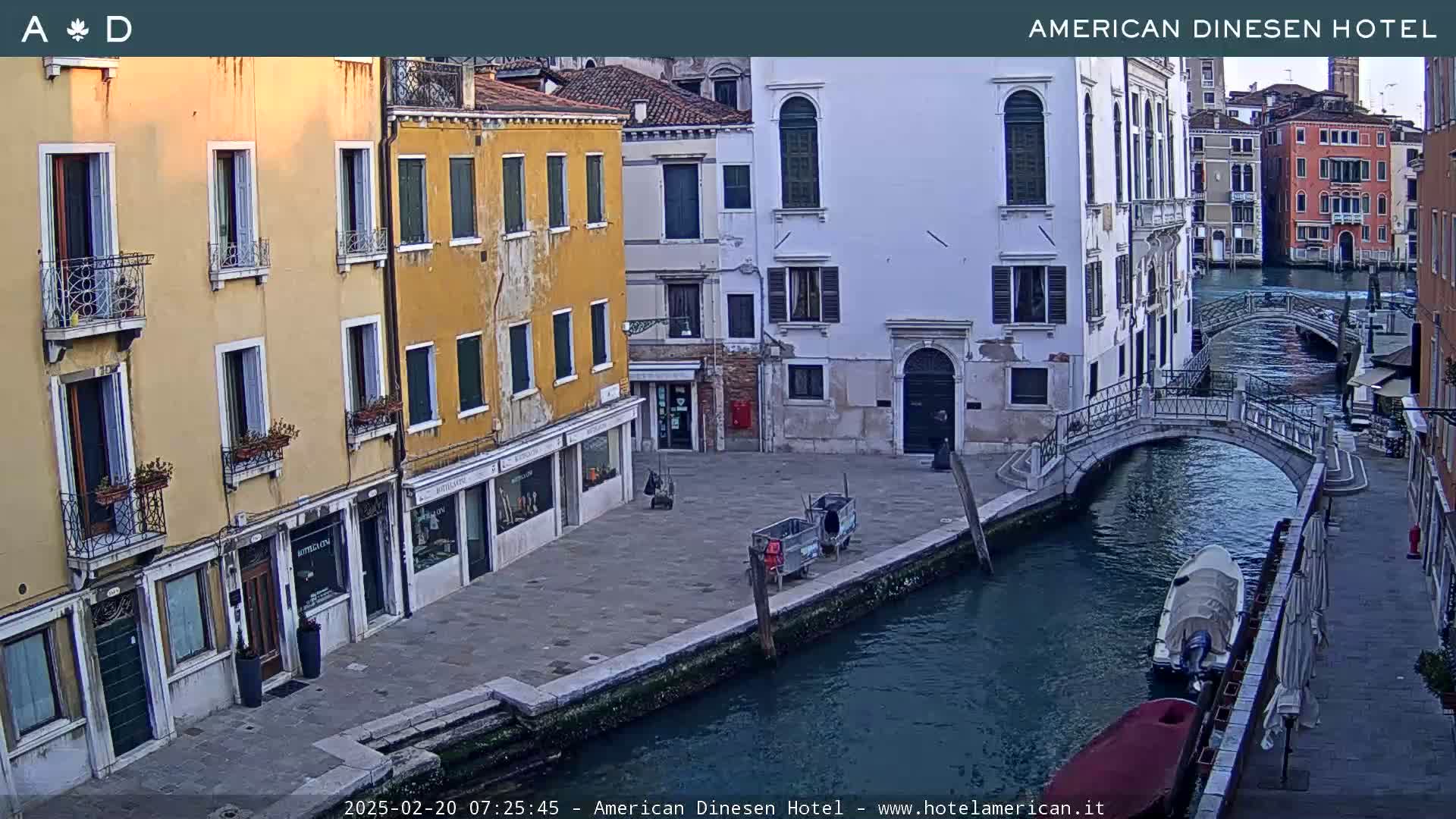A canal in Venice, Italy, with several buildings lining its banks, shows a mostly clear day with some shadows.