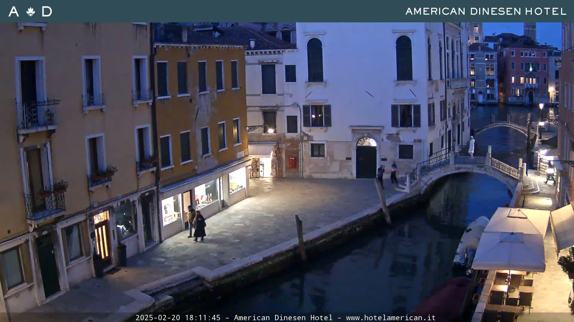 A twilight view of a canal in Venice, with stone buildings lining the waterway and a small bridge spanning the canal.