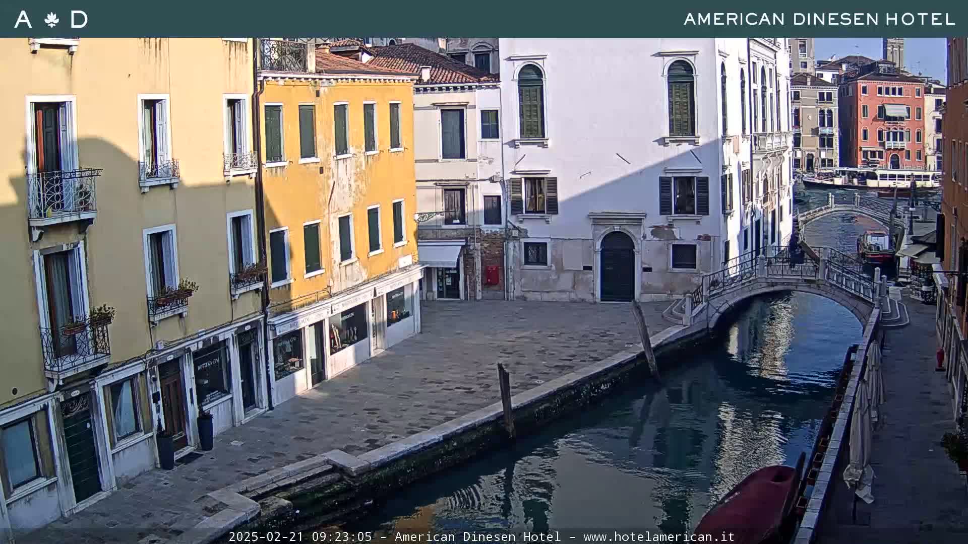 A sunny day in Venice shows colorful buildings lining a canal, with a small bridge and a gondola visible.