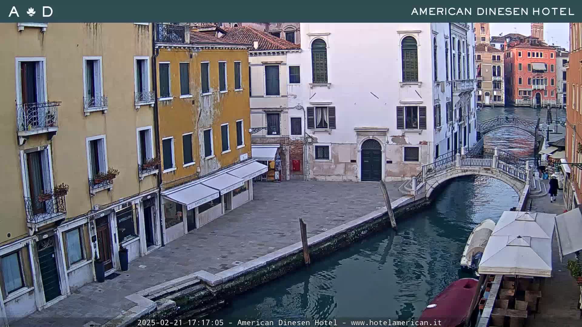 A view of a canal in Venice, Italy, shows several buildings lining the waterway with a small bridge crossing the canal, under a cloudy sky.