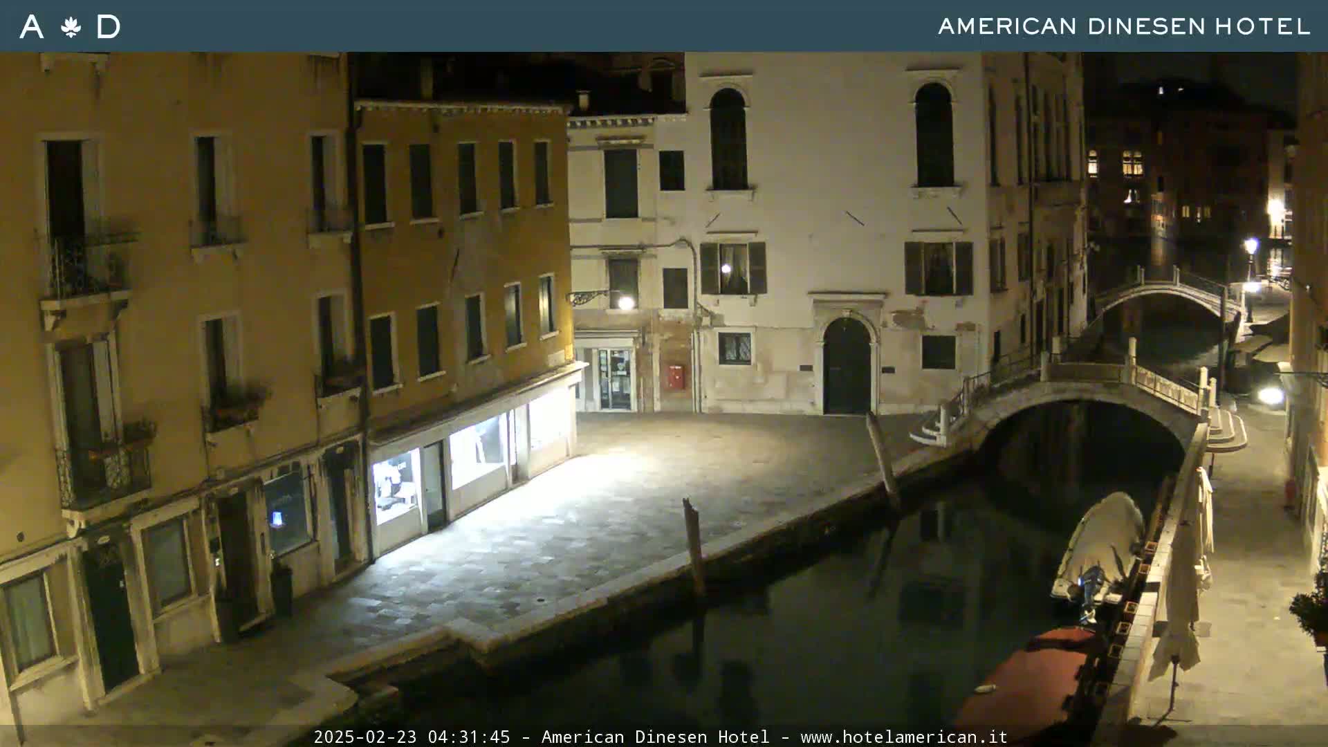A nighttime view of a canal in Venice, showing several buildings along the waterway and a small bridge.