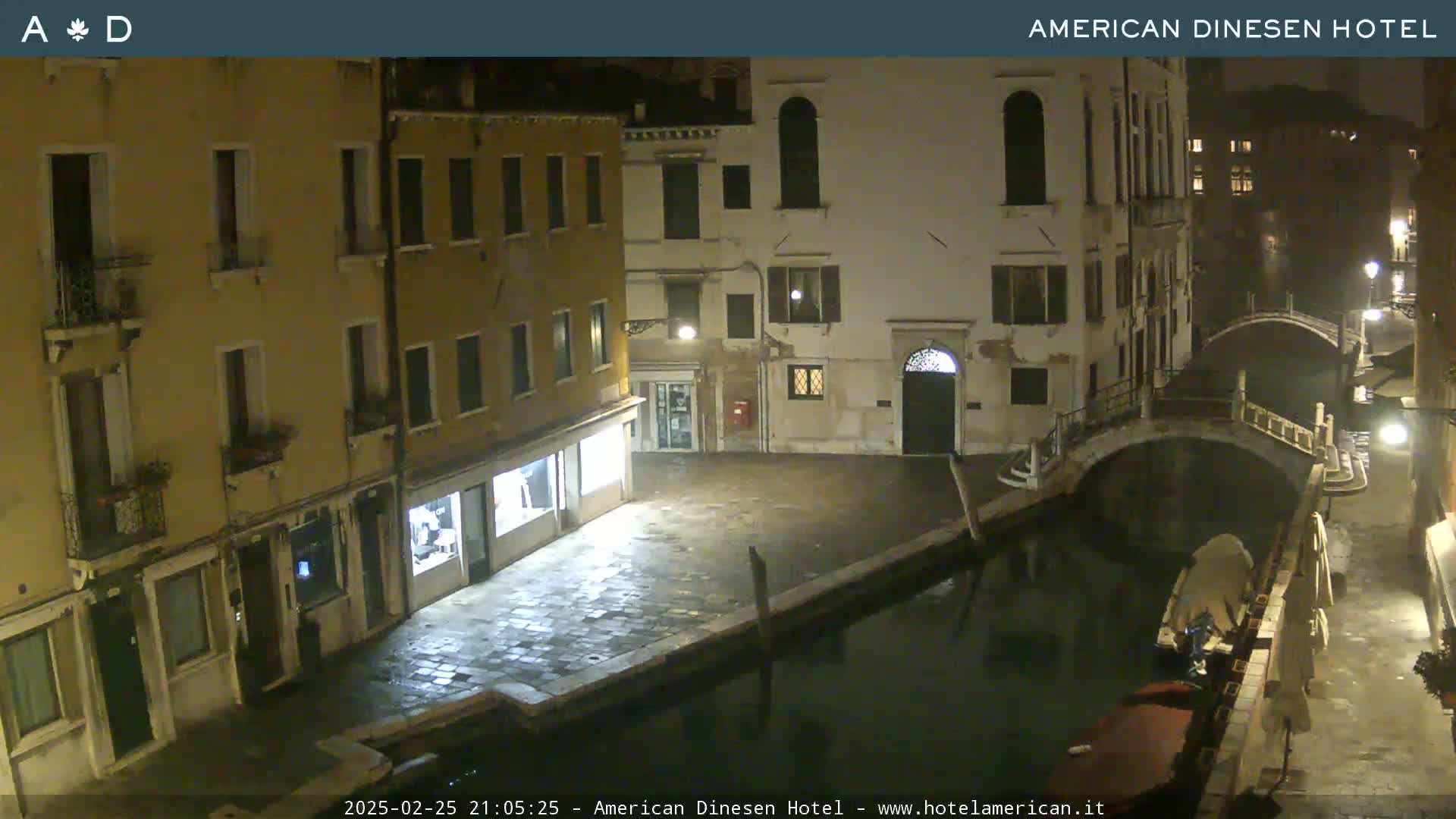 A nighttime view of a canal in Venice, with buildings lining the waterway and a small bridge visible.