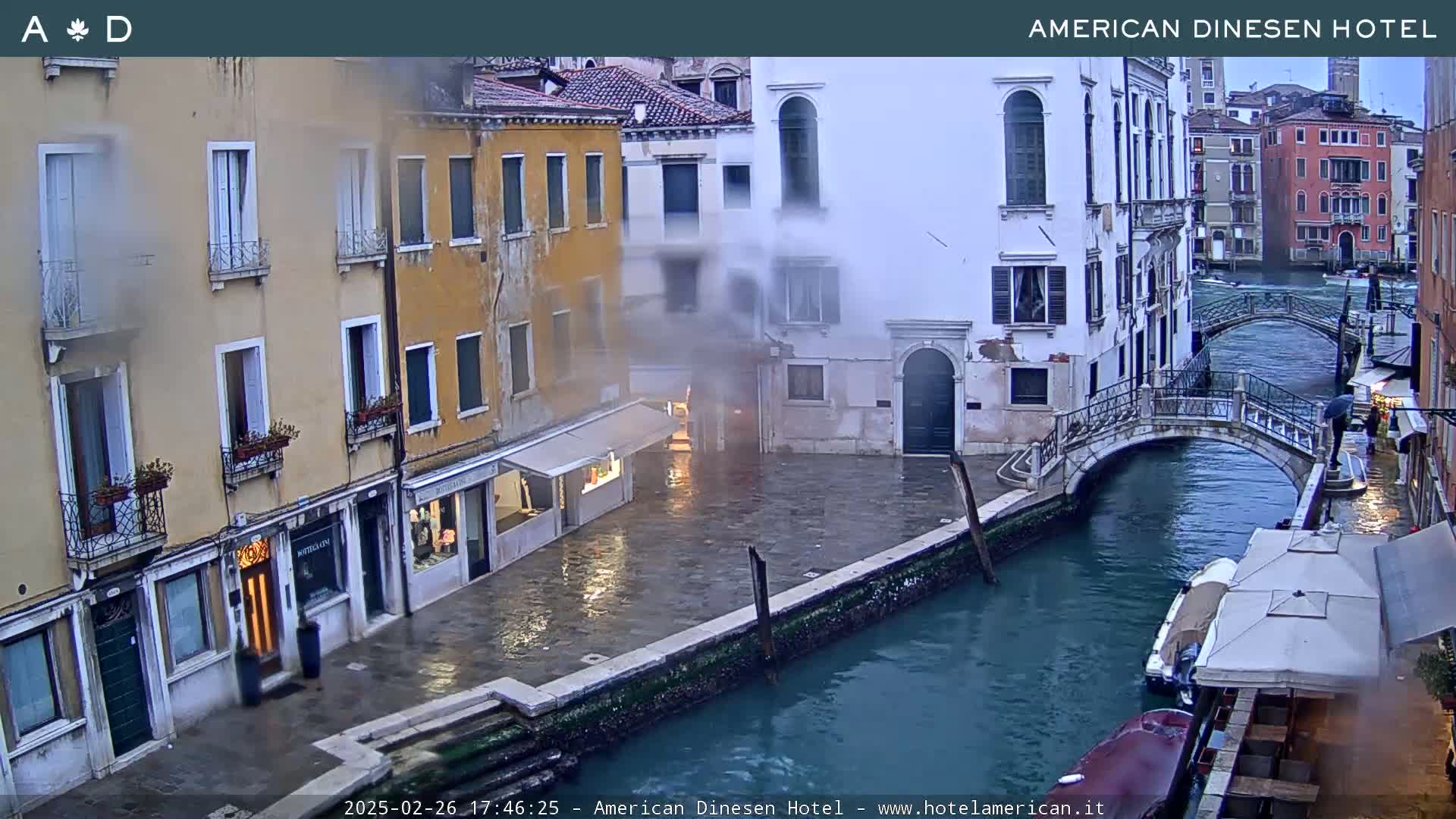 A misty view of a canal in Venice, with colorful buildings lining the waterway and a small bridge spanning the canal.