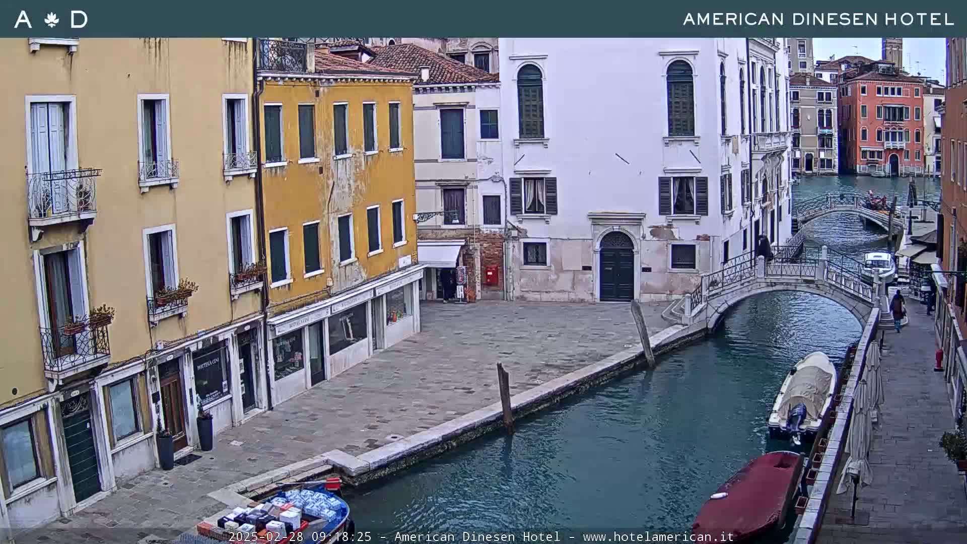 A canal in Venice, Italy, with several buildings lining its banks and small boats moored along the waterway, under overcast skies.