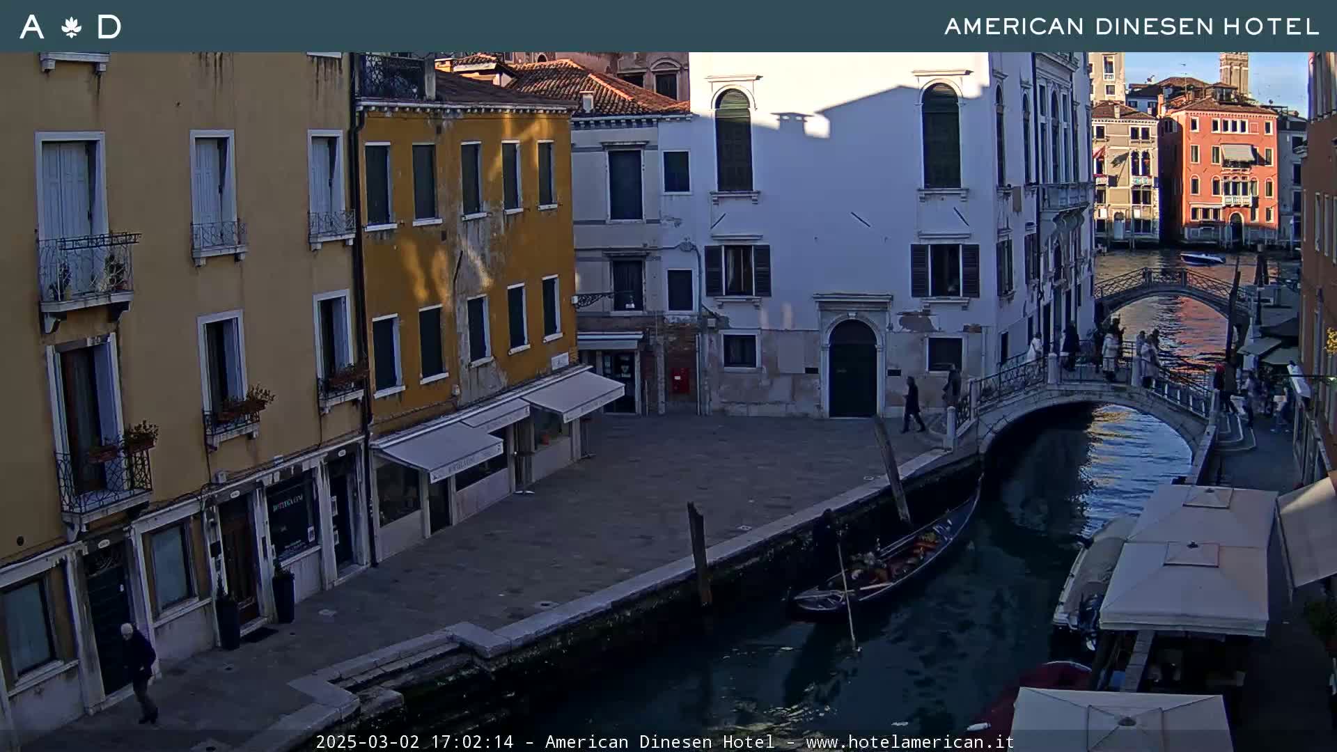 A gondola is on a canal in Venice, Italy, under a partly sunny sky, next to buildings and a bridge with people walking on it.