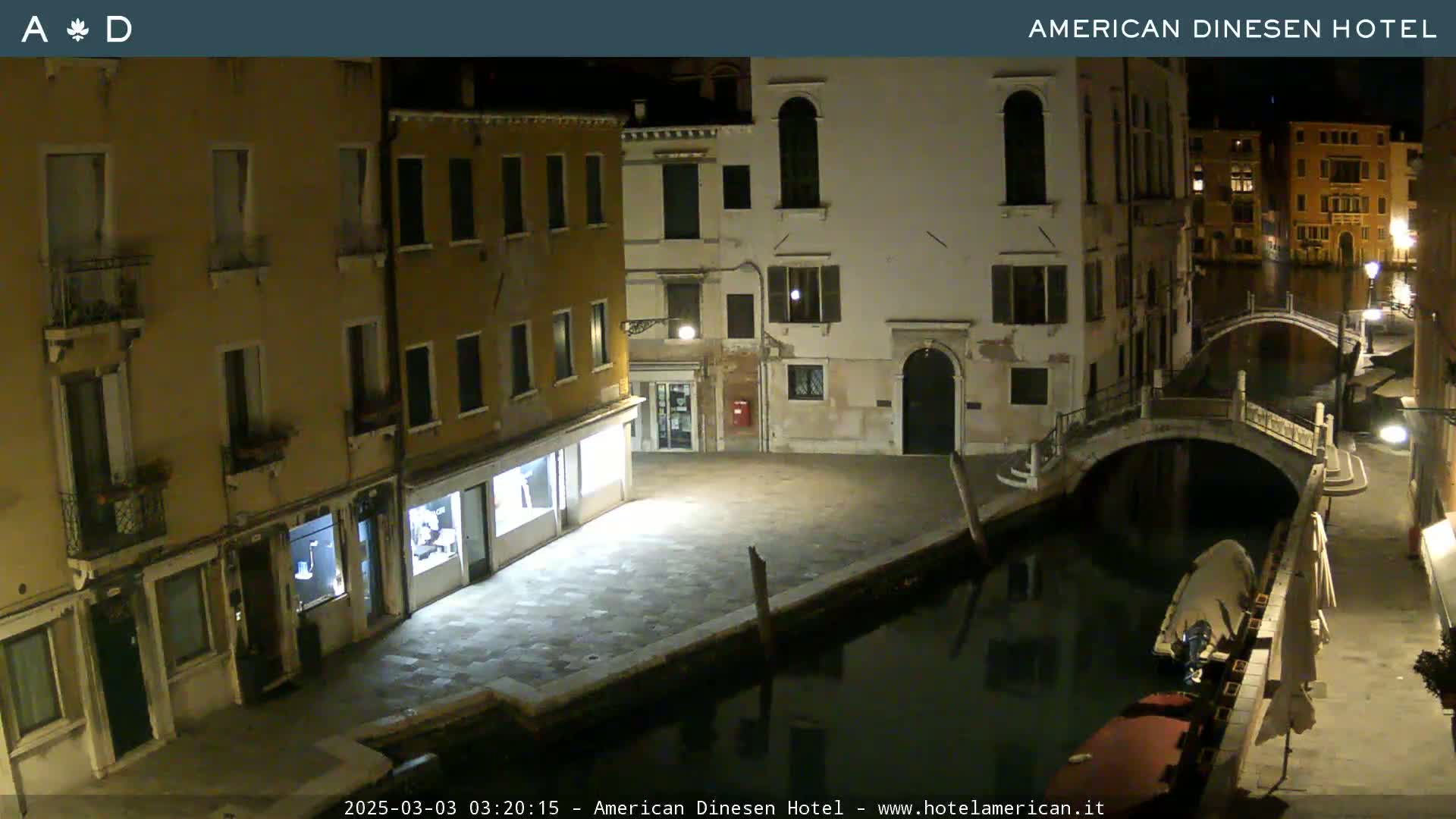 A nighttime view of a canal in Venice, with several buildings lining the waterway and a small bridge visible.