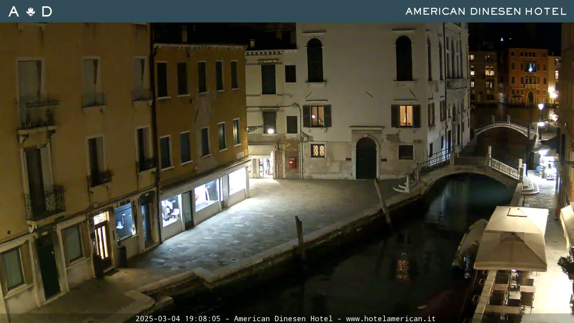 A nighttime view of a canal in Venice, showing several buildings lining the waterway and a small bridge spanning the canal.