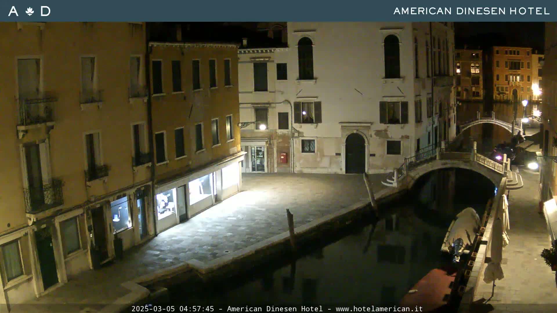 A nighttime view of a canal in Venice, Italy, showing several buildings lining the waterway and a small bridge spanning the canal.