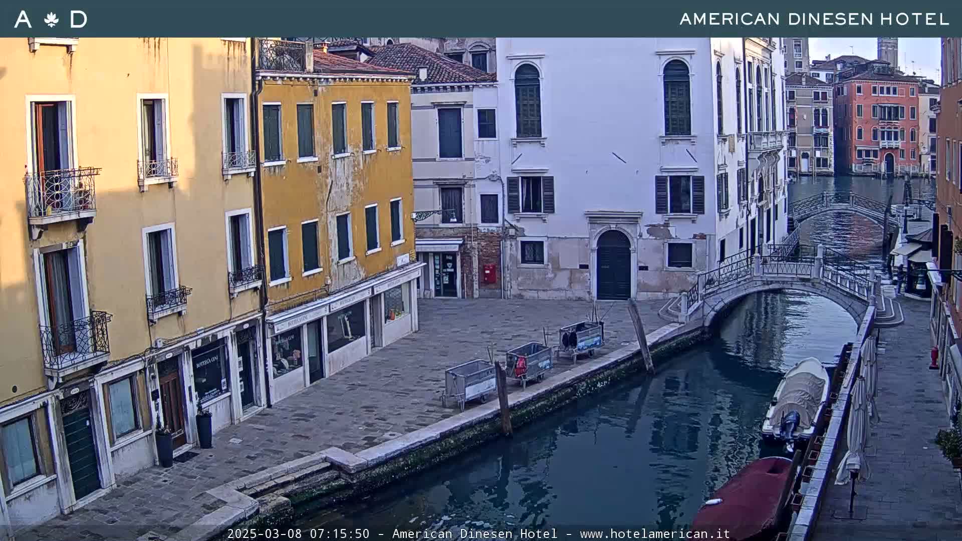 A calm canal in Venice, Italy, is lined with pastel-colored buildings under a clear, bright sky.
