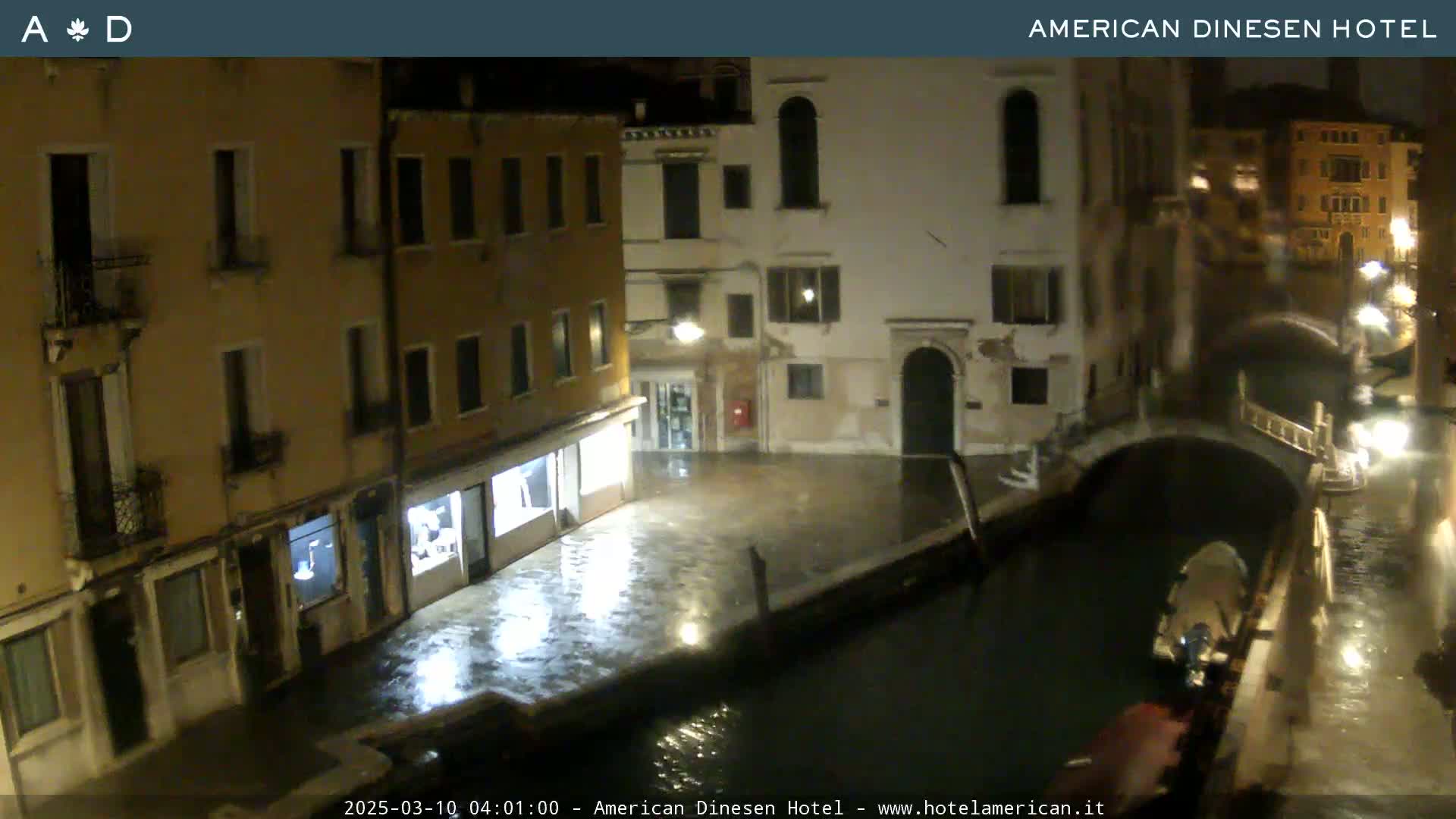 A nighttime view of a canal in Venice, showing several buildings lining the waterway under wet, rainy conditions.