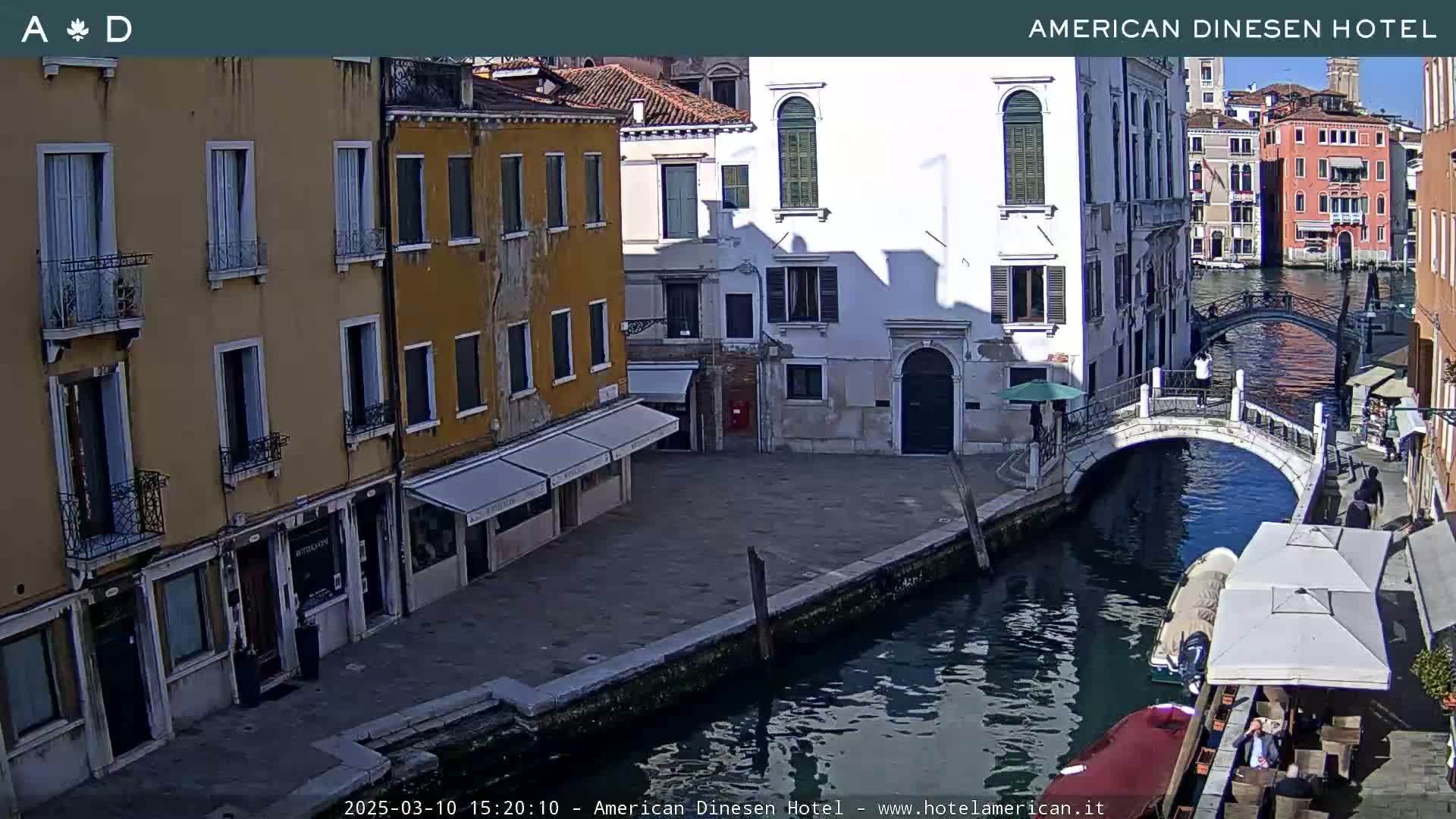 A sunny view of a canal in Venice, Italy, with colorful buildings lining the waterway and a small bridge connecting the opposite banks.