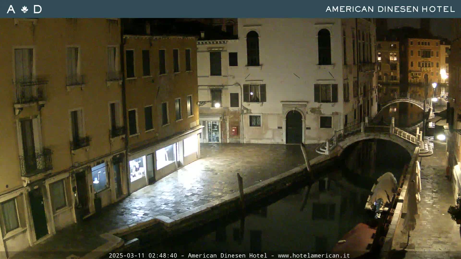 A nighttime view of a canal in Venice, with several buildings lining the waterway and a small bridge spanning the canal.