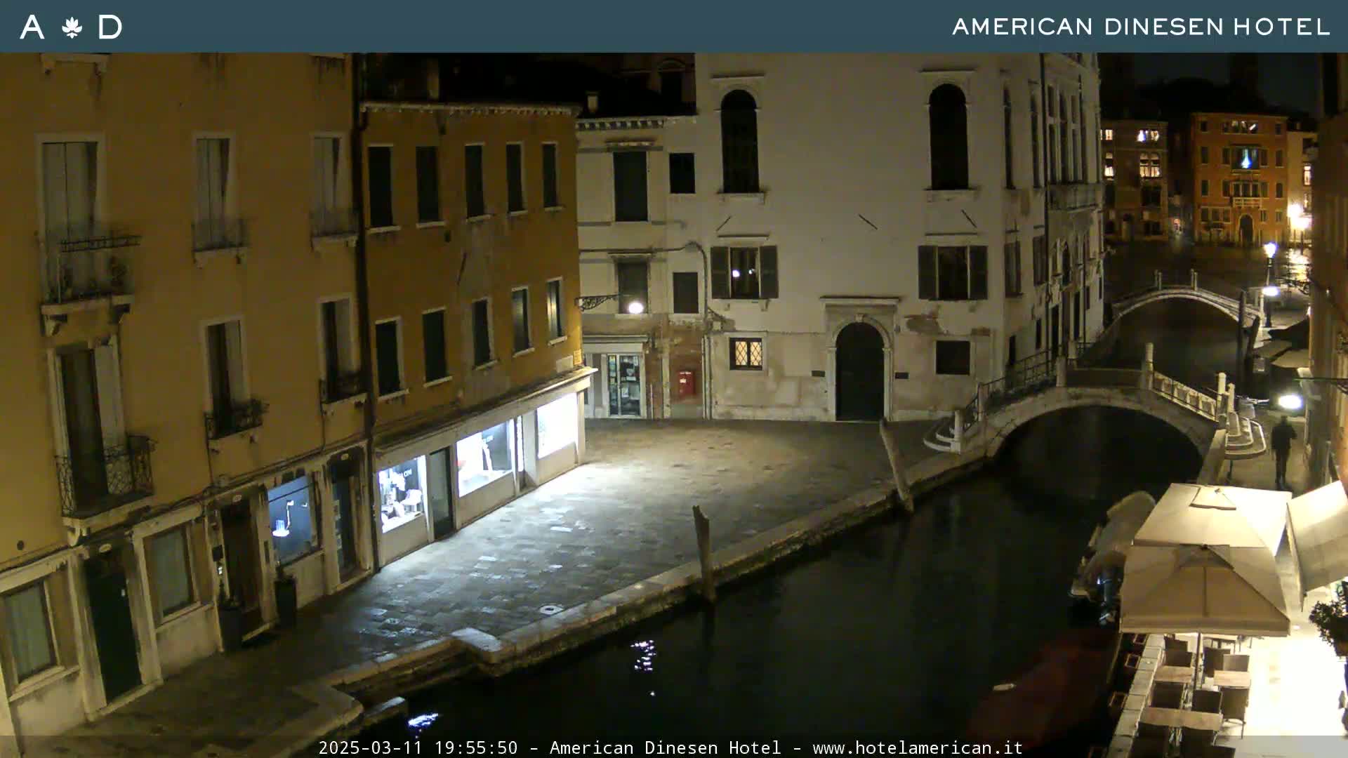 A nighttime view of a canal in Venice, showing several buildings along the waterway and a small bridge.