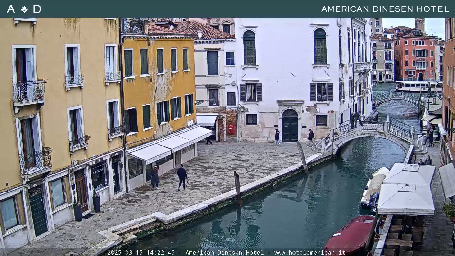 A tranquil canal scene in Venice, showing several buildings and a small footbridge, under an overcast sky.
