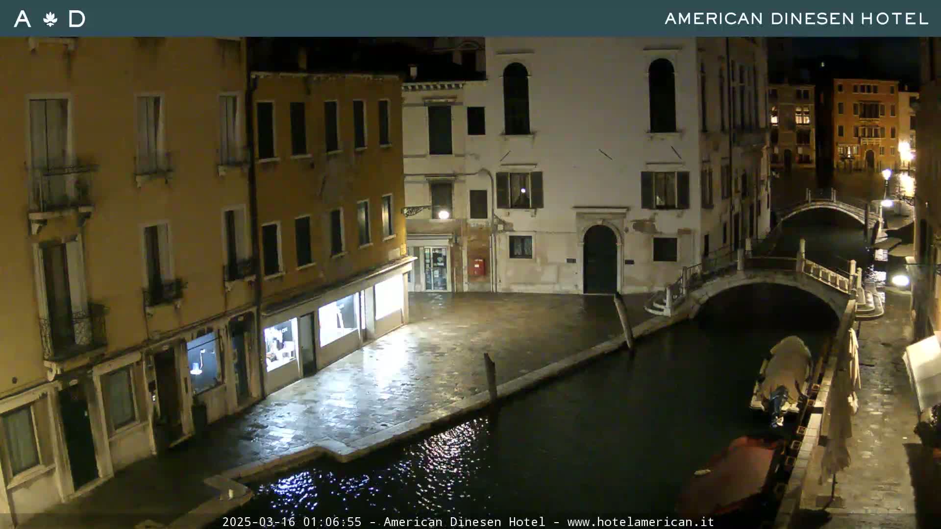A nighttime view of a canal in Venice, showing buildings lining the waterway and a small bridge, with a boat moored nearby.