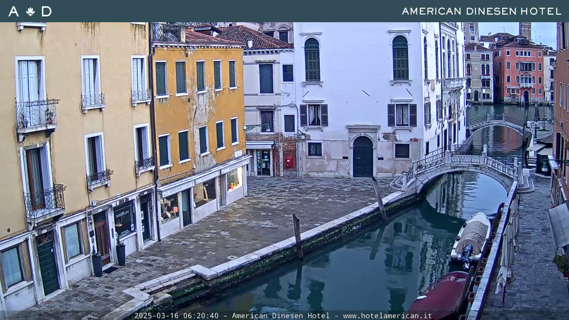 A calm canal in Venice, with several buildings lining its banks and a small boat moored alongside a bridge.