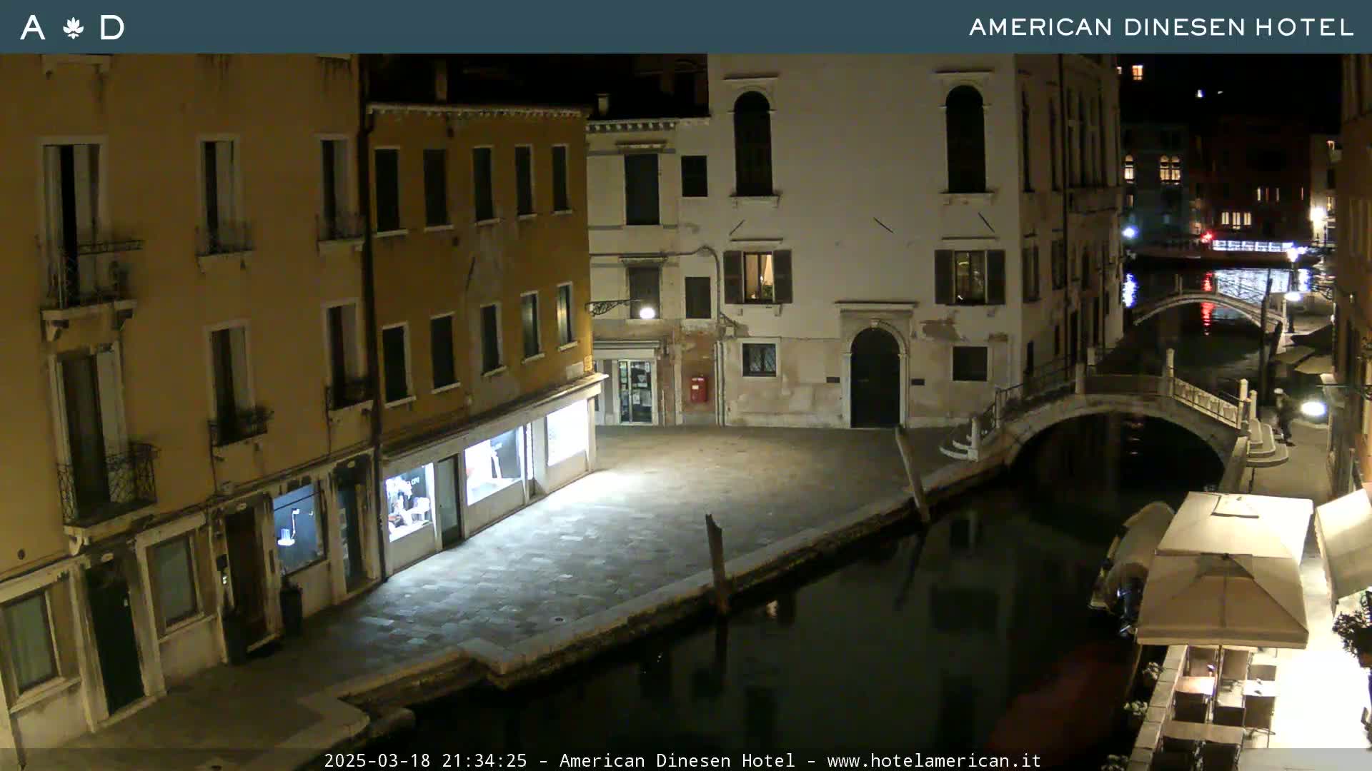 A nighttime view of a canal in Venice, with buildings lining the waterway and a bridge in the distance under a clear, dark sky.