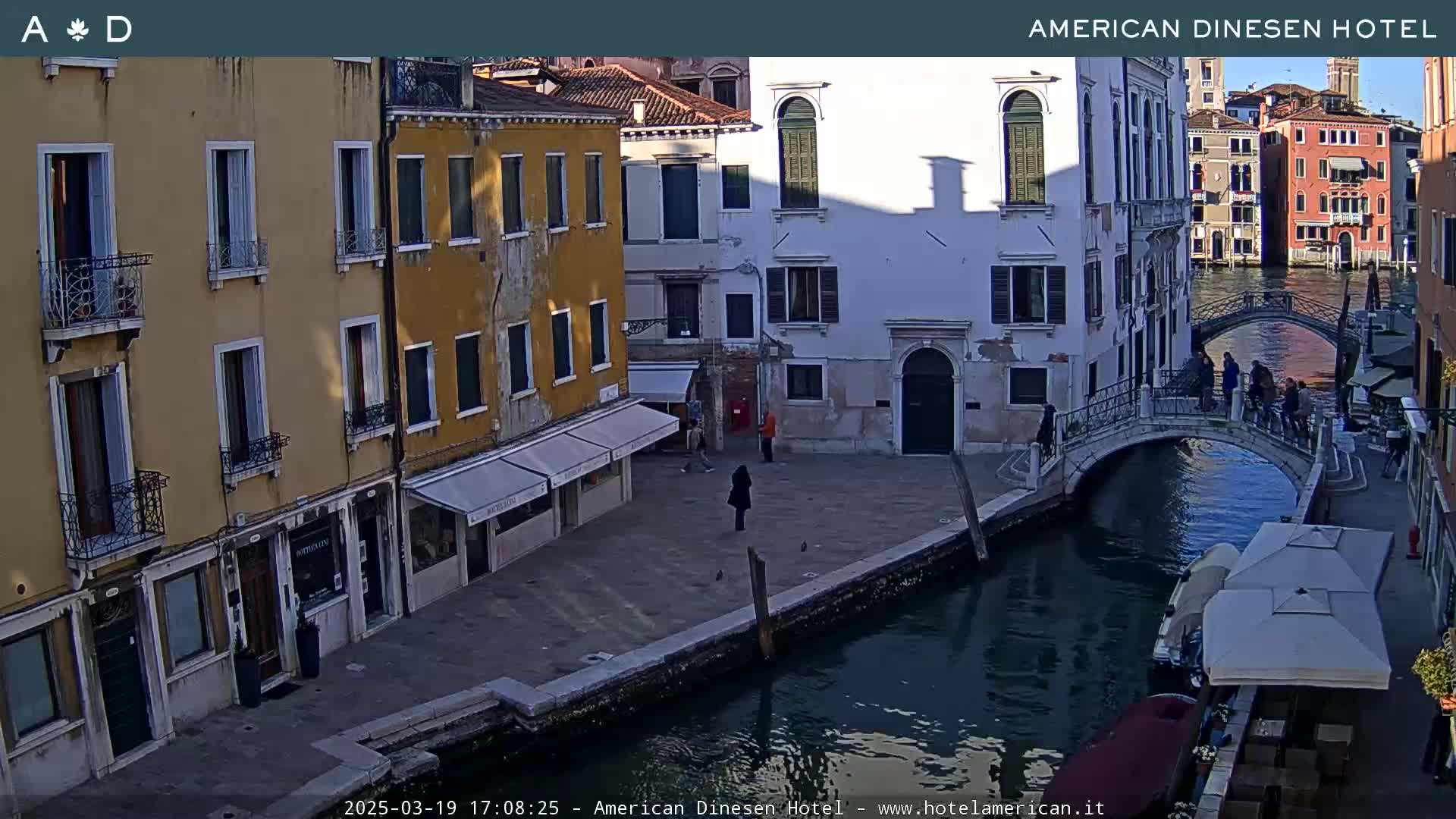 A sunny view of a canal in Venice, with colorful buildings lining the waterway and a small bridge connecting the two sides.