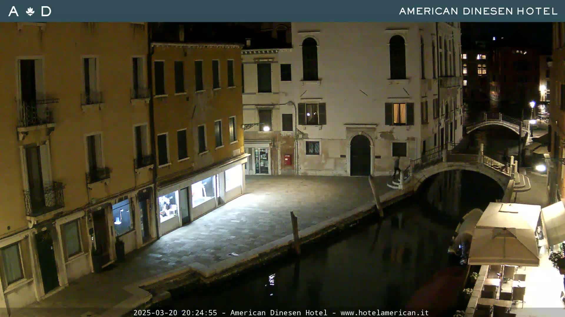 A nighttime view of a canal in Venice, with buildings lining the waterway and a small bridge crossing the canal.