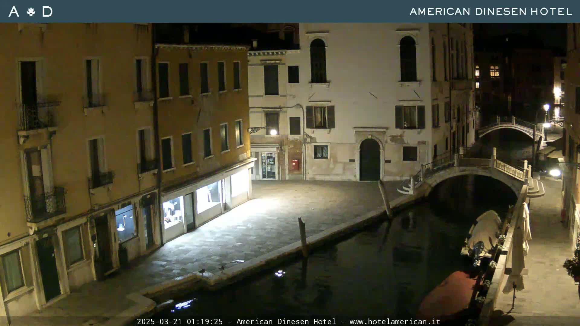 A nighttime view of a canal in Venice, with stone buildings lining the waterway and a small bridge visible.