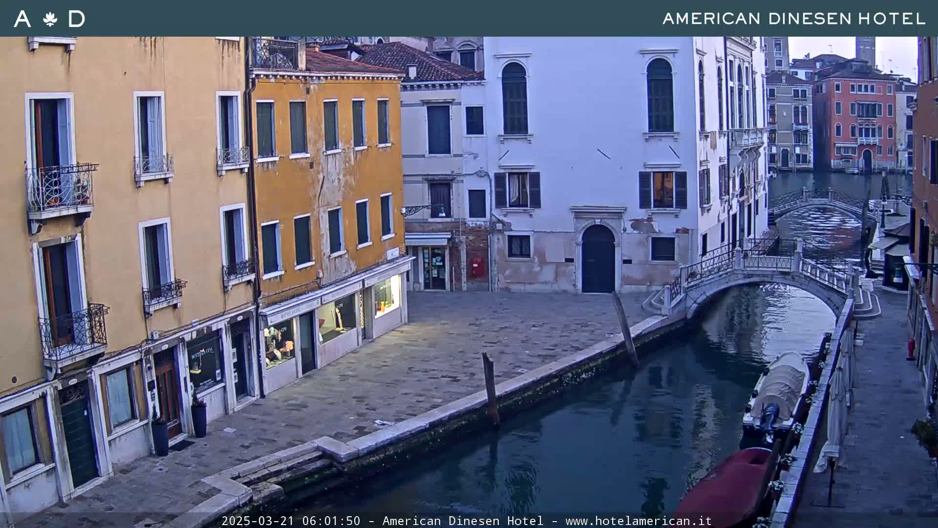 A canal in Venice, Italy, at dusk, shows several buildings lining its banks, with a small bridge and a boat moored on the water.