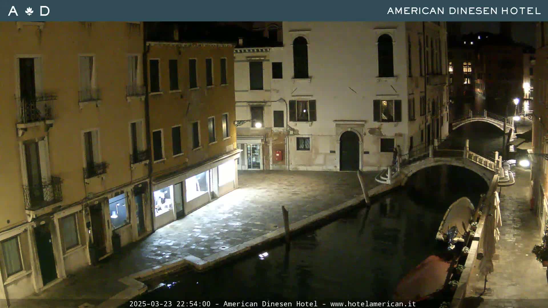 A nighttime view of a canal in Venice, Italy, with several buildings lining the waterway and a small bridge crossing the canal.