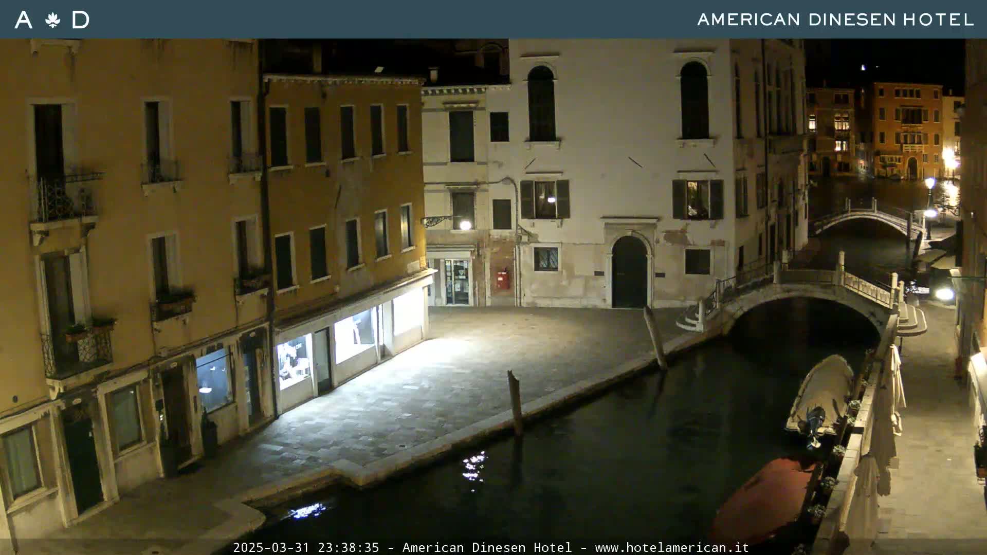 A nighttime view of a canal in Venice, showing several buildings and a small bridge, under a clear, moonlit sky.