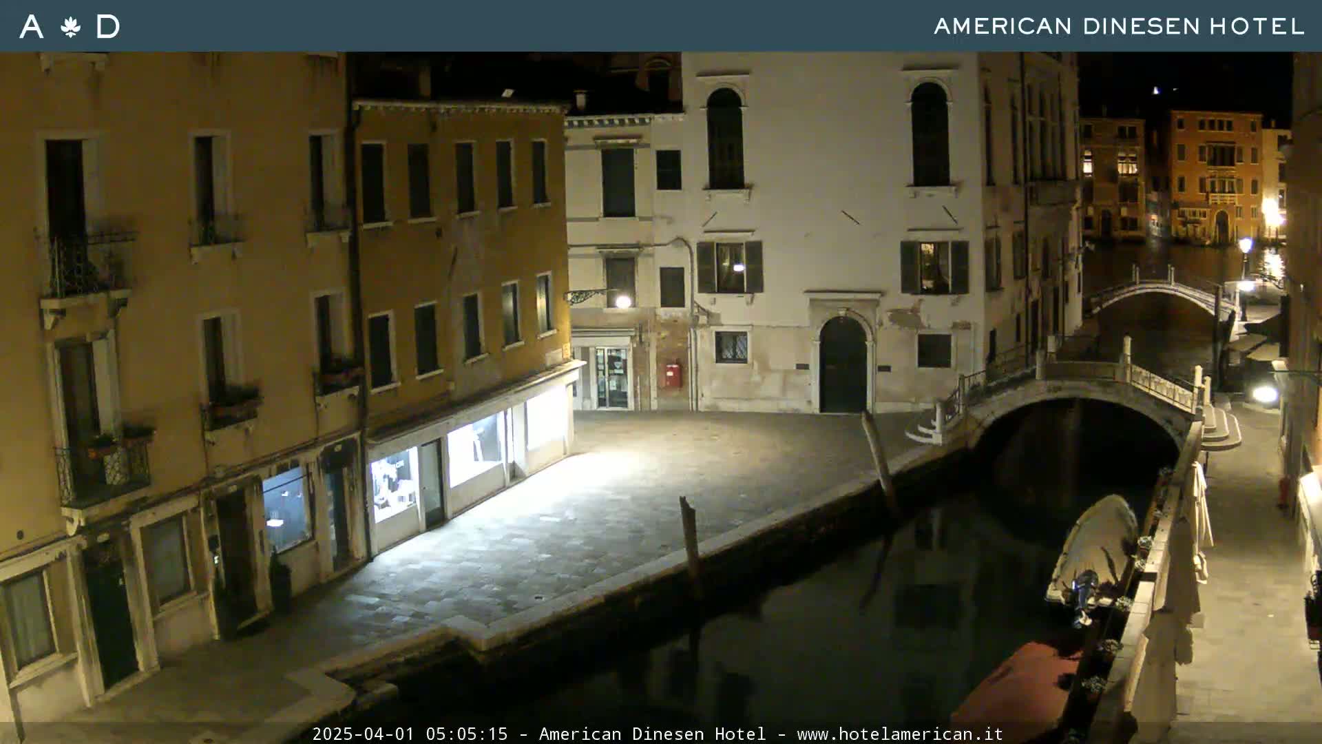 A nighttime view of a canal in Venice, showing buildings lining the waterway and a small bridge spanning the canal.