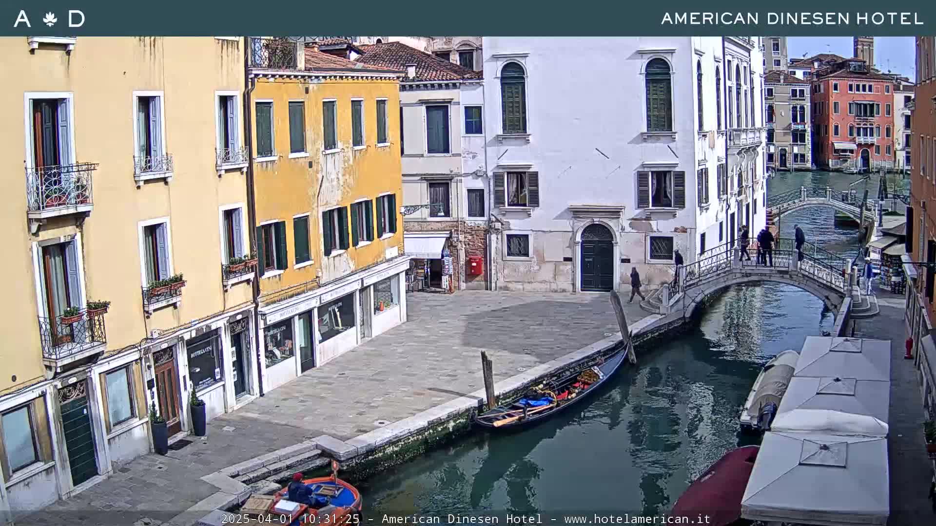 A sunny day in Venice shows a canal with gondolas, pedestrians crossing a bridge, and colorful buildings lining the waterway.