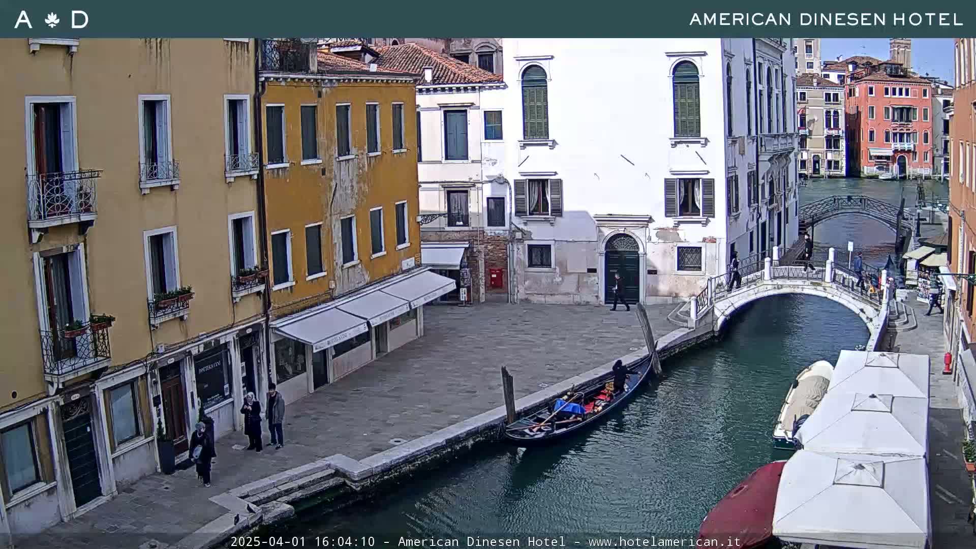 A gondola floats on a canal in Venice, Italy, under a sunny sky, alongside buildings and a pedestrian bridge.