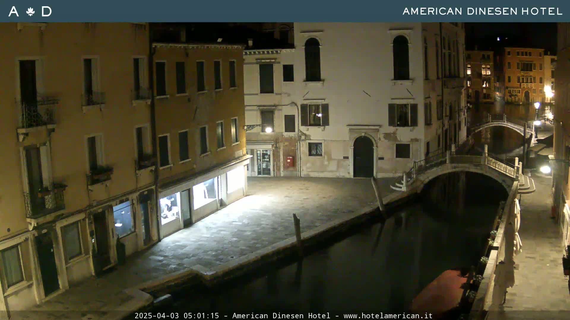 A nighttime view of a canal in Venice, with several buildings lining the waterway and a small bridge visible.