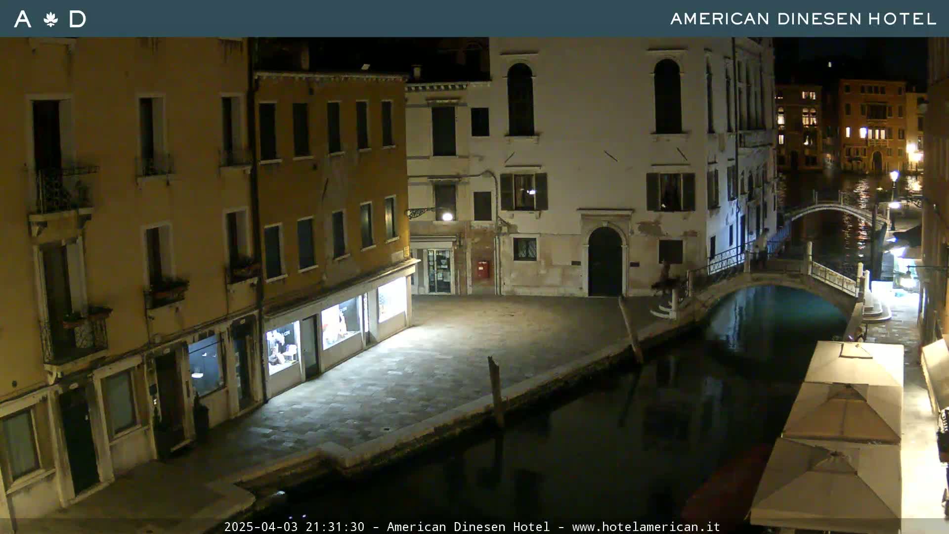 A nighttime view of a canal in Venice, showing several buildings lining the waterway and a small bridge crossing the canal.