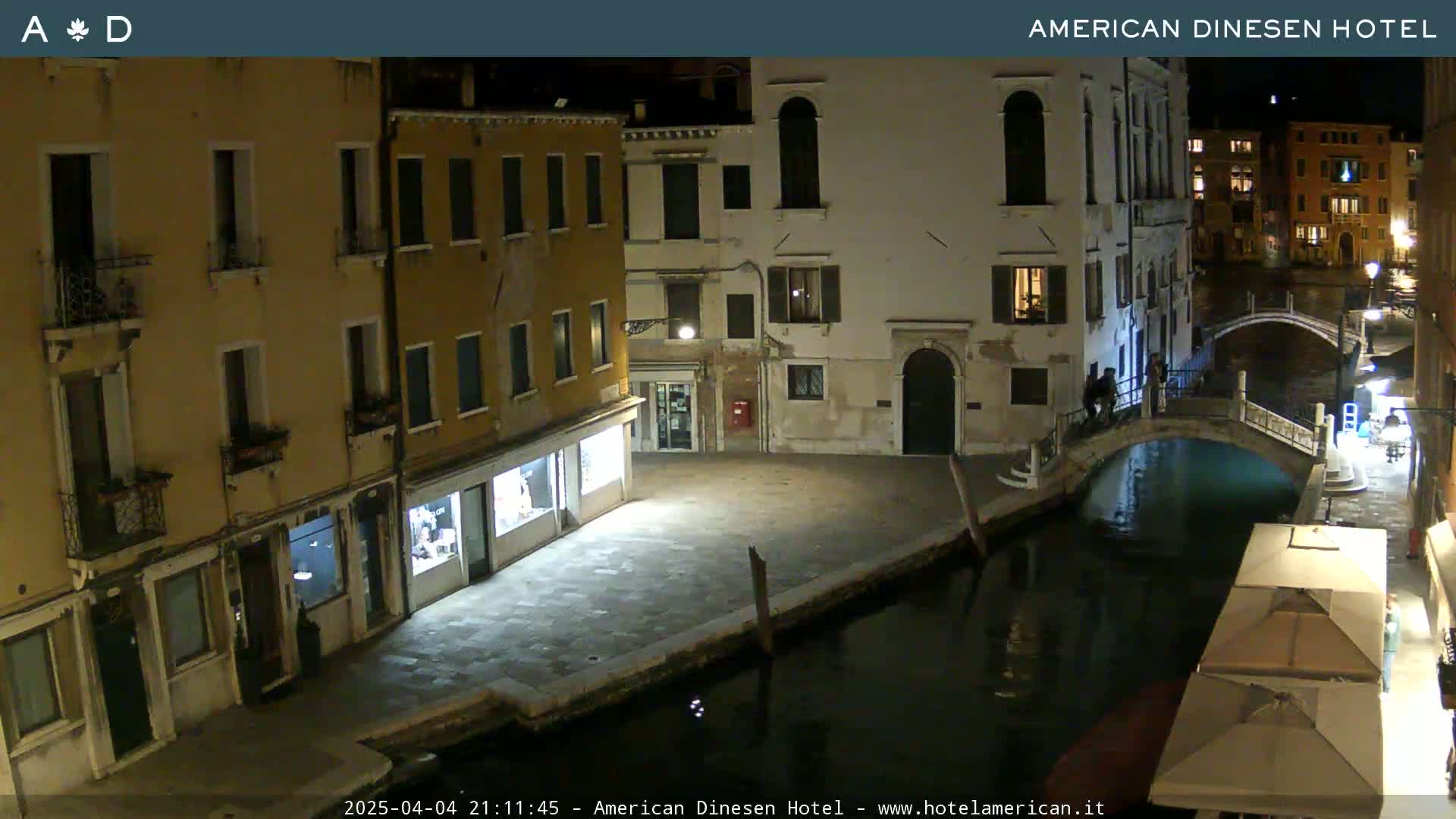 A nighttime view of a canal in Venice, Italy, with buildings lining the waterway and a small bridge crossing the canal.