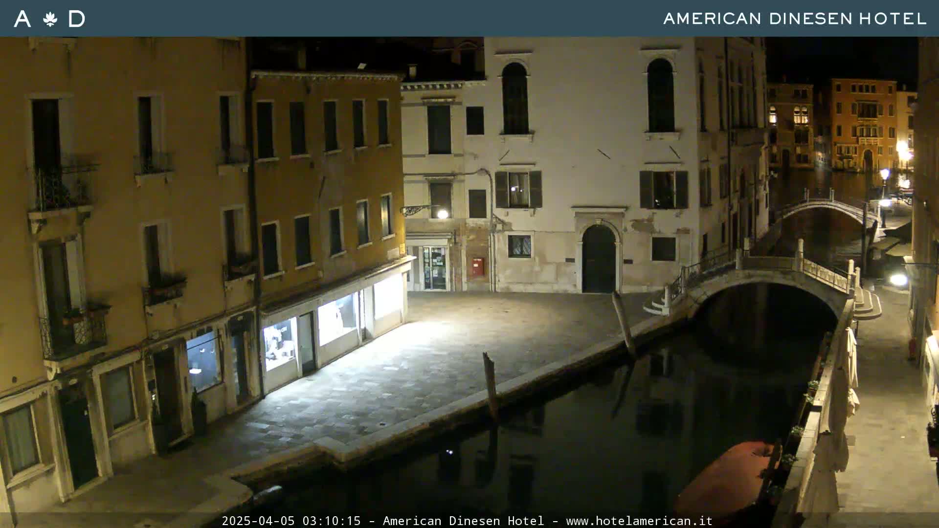 A nighttime view of a canal in Venice, showing several buildings lining the waterway and a small bridge crossing the canal.