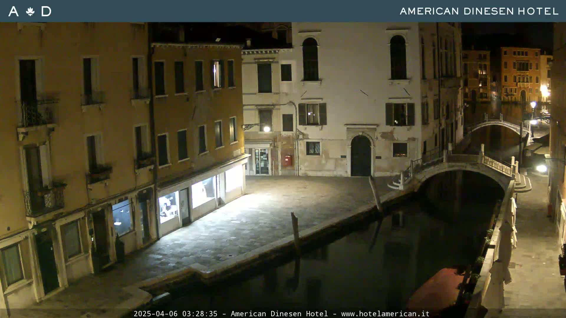 A nighttime view of a canal in Venice, Italy, showing several buildings along the waterway and a small arched bridge spanning the canal.