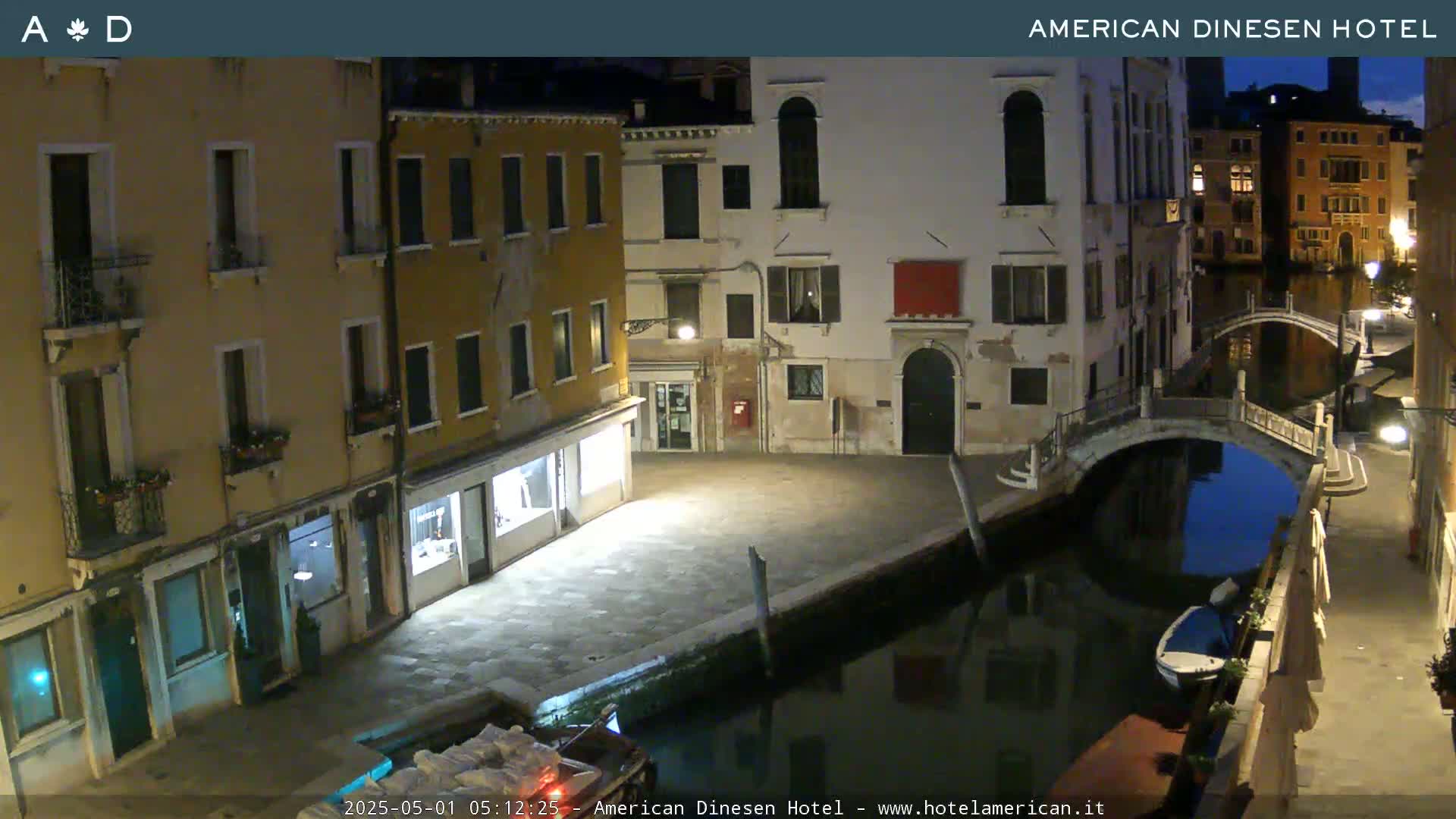 A nighttime view of a canal in Venice, with several buildings lining the waterway and a small bridge crossing the canal.