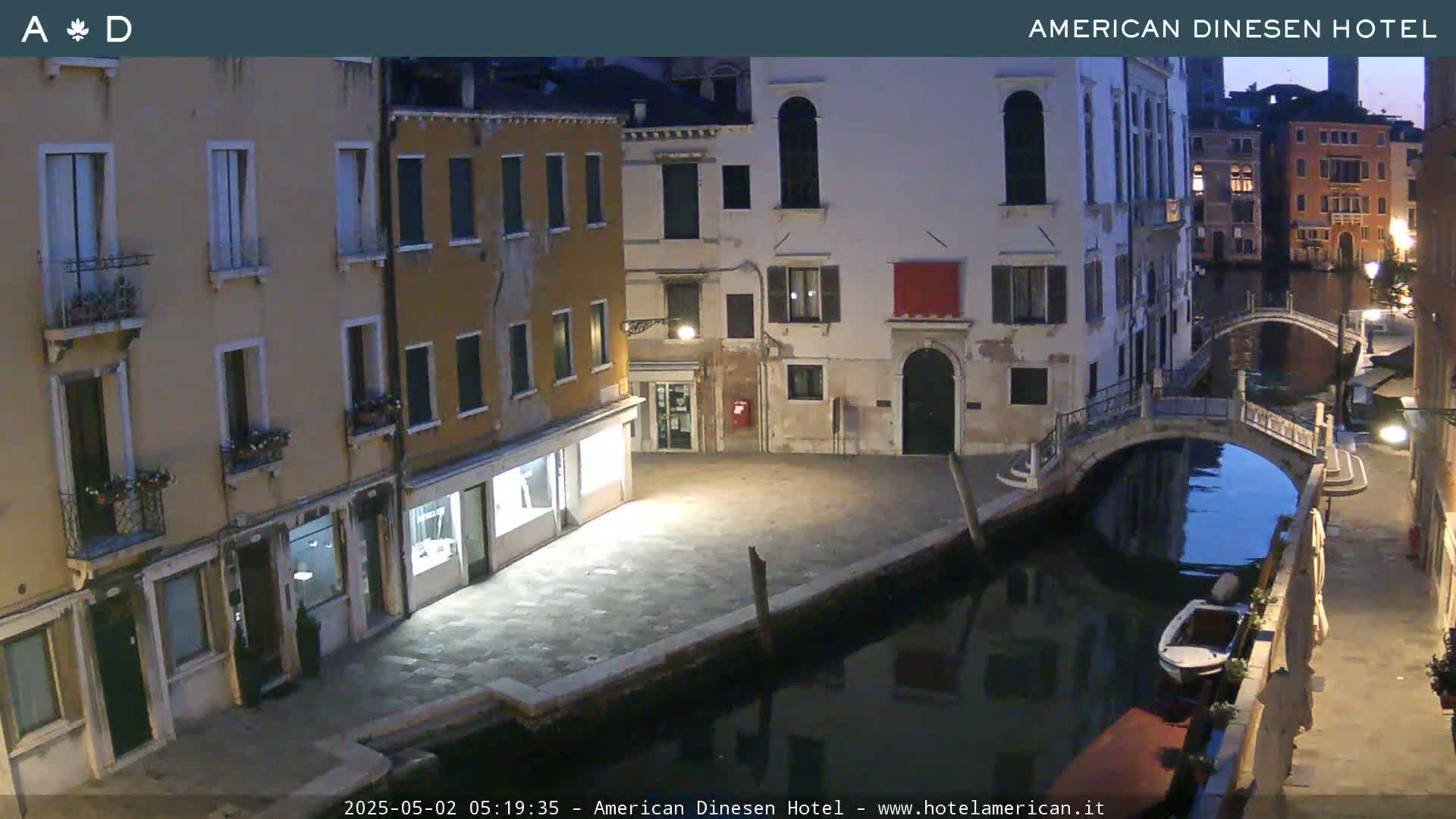 A nighttime view of a canal in Venice, showing buildings lining the waterway and a small boat moored alongside a bridge.