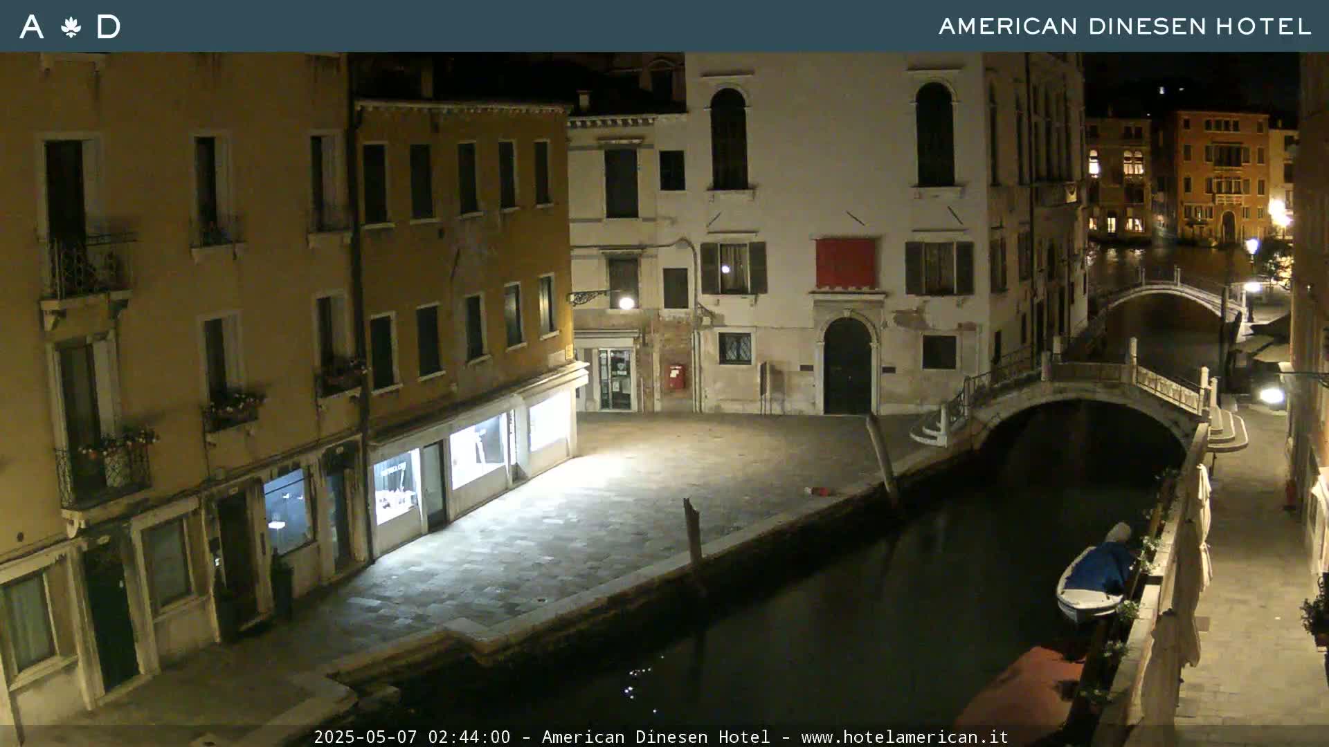 A nighttime view of a canal in Venice, with several buildings lining the waterway and a small bridge spanning the canal.