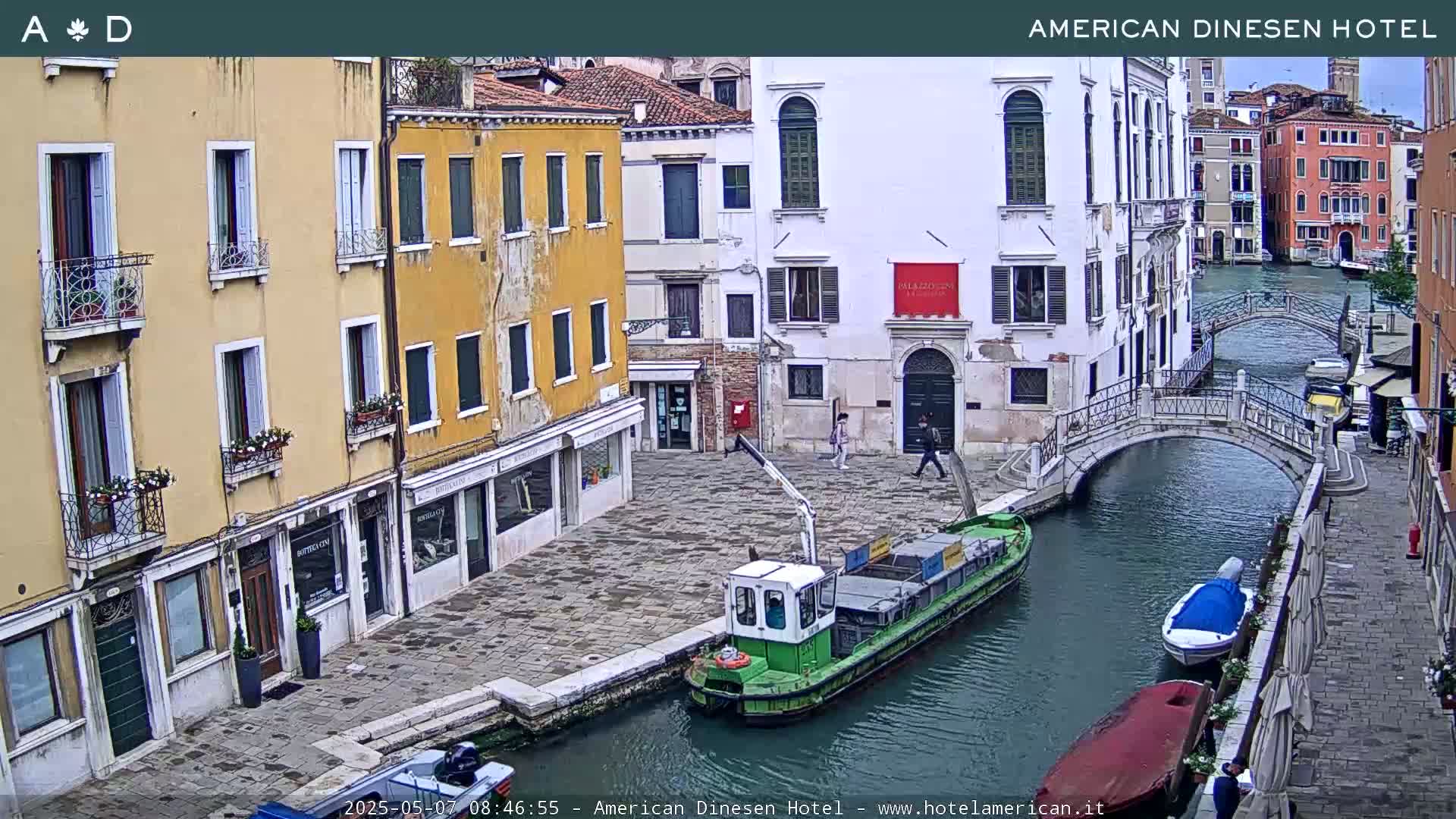 A canal in Venice, Italy, with several buildings lining its banks, a small barge on the water, and a pedestrian bridge.