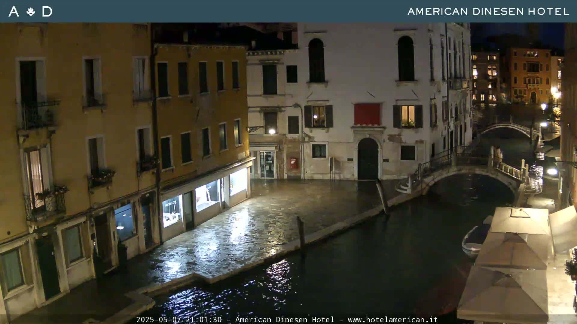 A nighttime view of a canal in Venice, showing several buildings along its banks and a small bridge spanning the waterway.