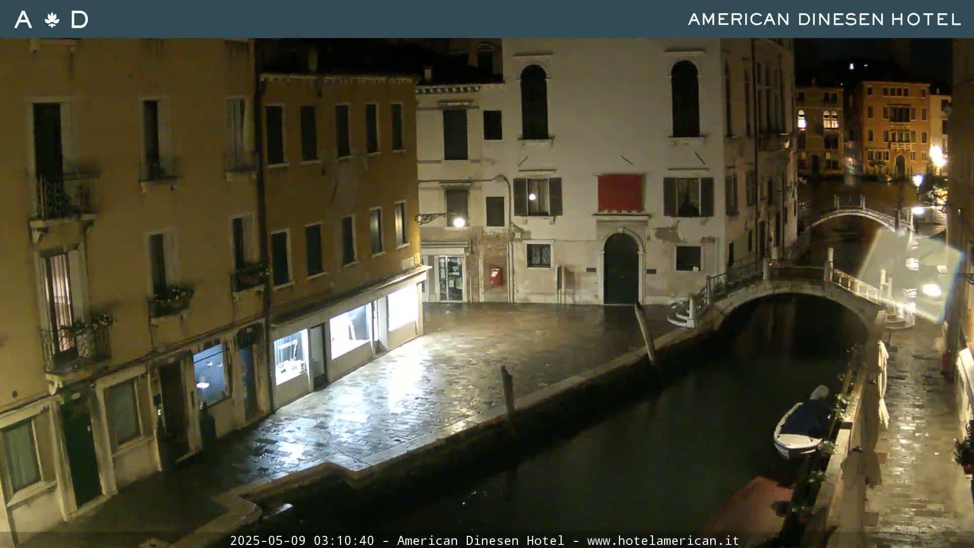 A nighttime view of a canal in Venice, showing several buildings and a small boat, under a clear sky.