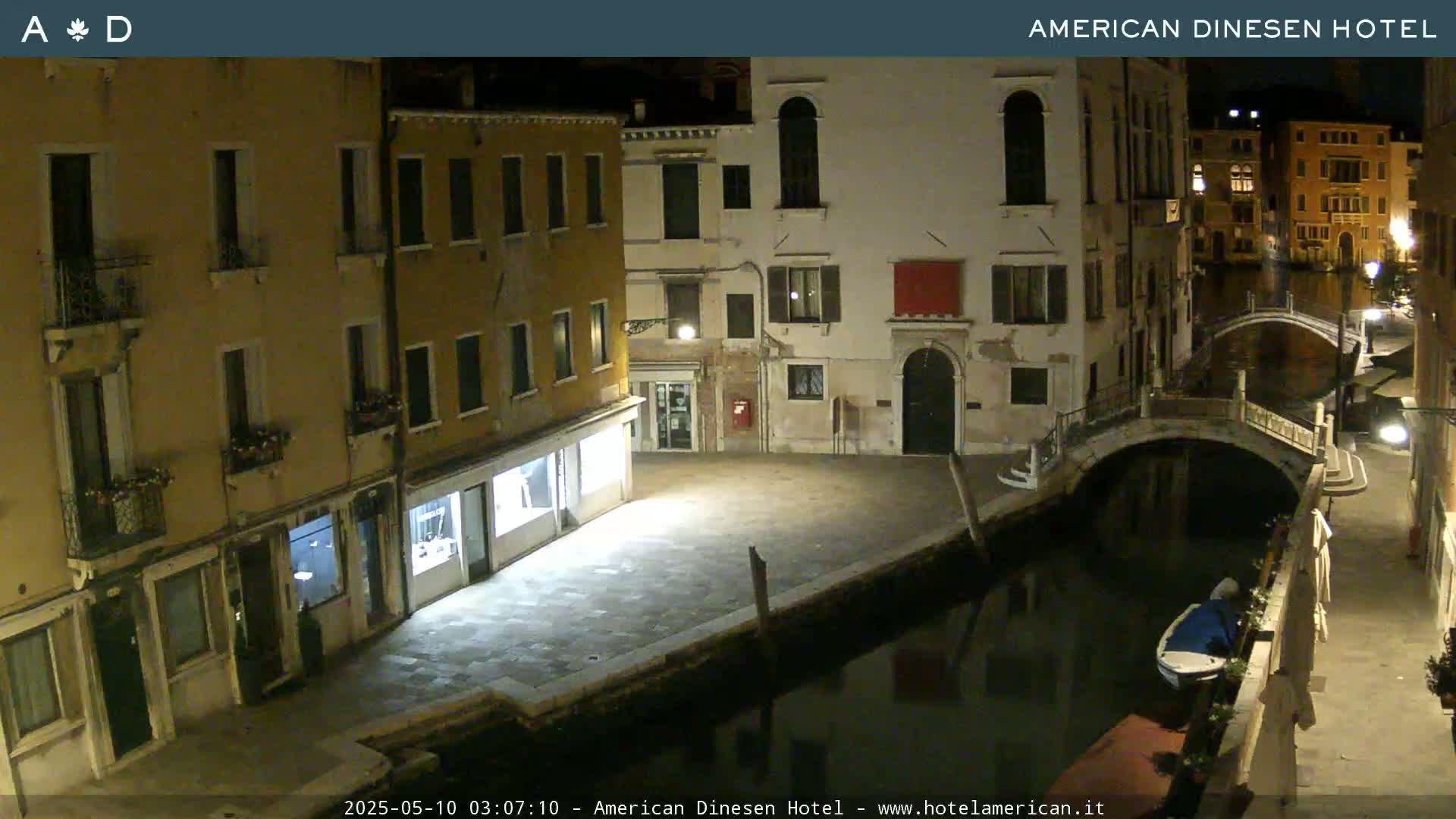 A nighttime view of a canal in Venice, showing buildings lining the waterway and a small bridge.