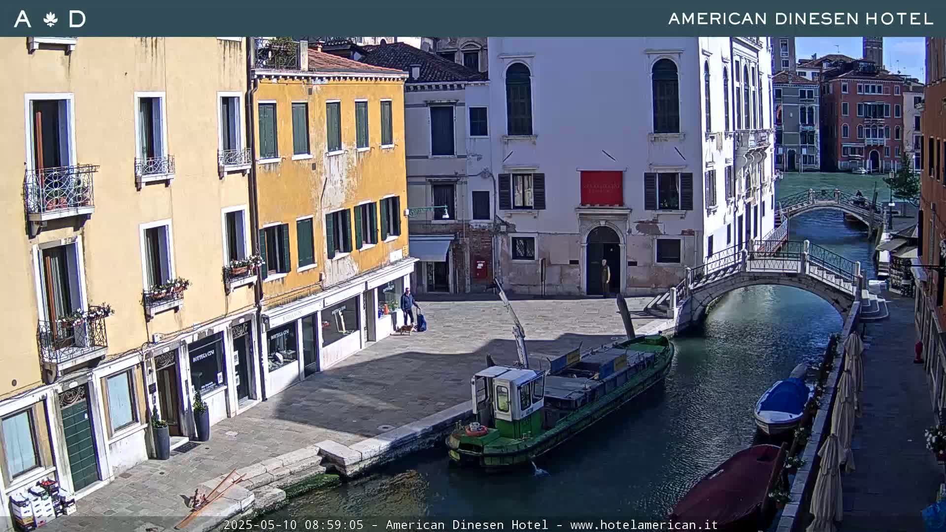 A sunny view of a canal in Venice, Italy, with colorful buildings lining the waterway and a barge moored along the quay.