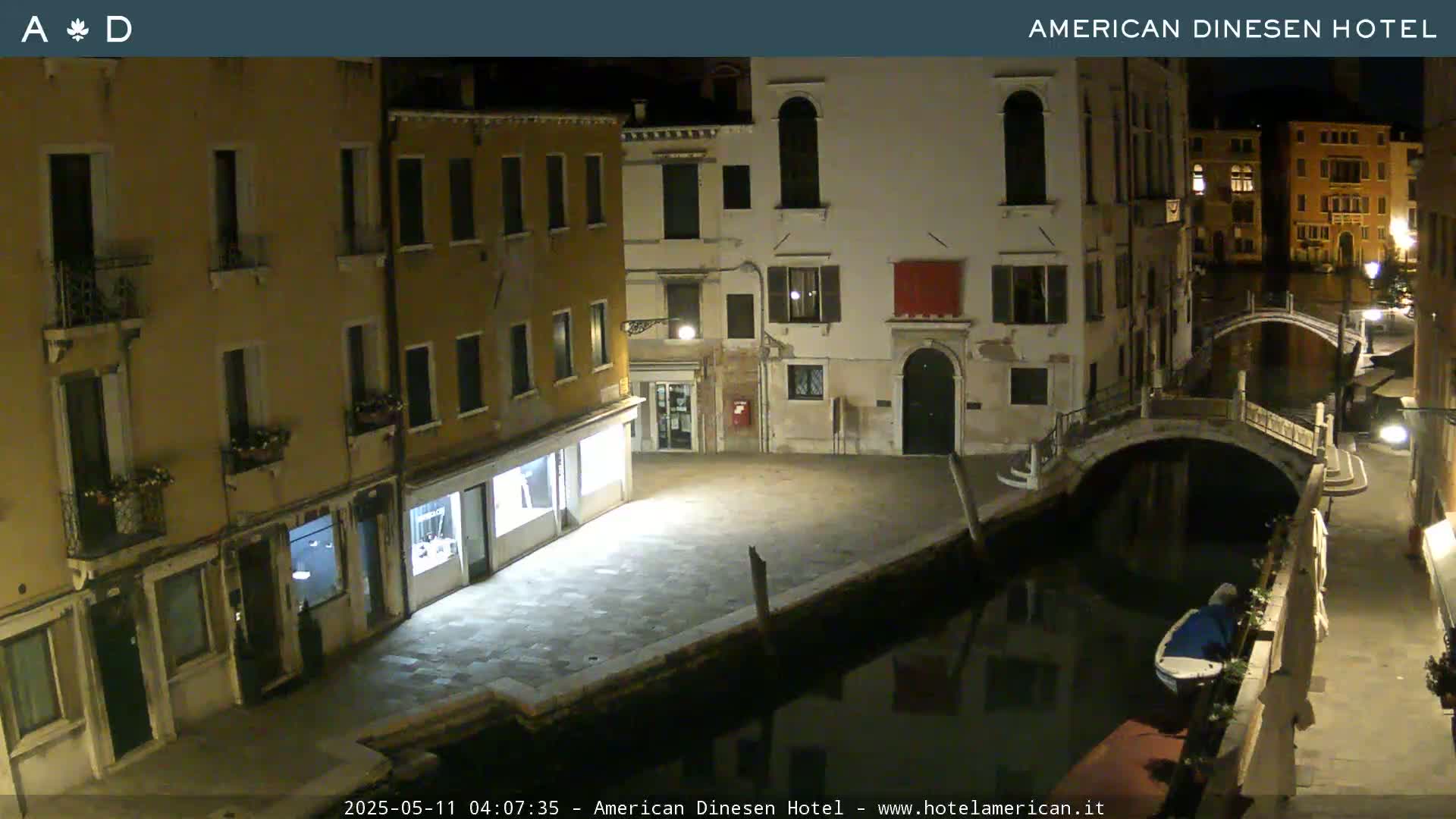 A nighttime view of a canal in Venice, showing buildings along the waterway and a small bridge, with a boat moored nearby.
