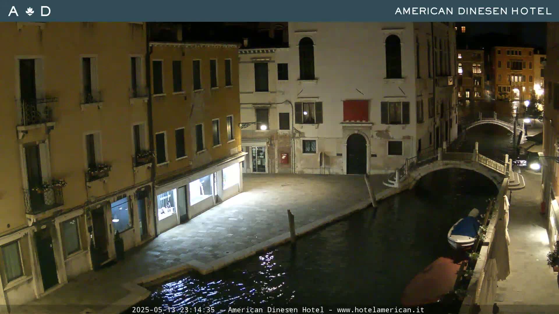 A nighttime view of a canal in Venice, showing buildings lining the waterway and a small boat moored near a bridge.