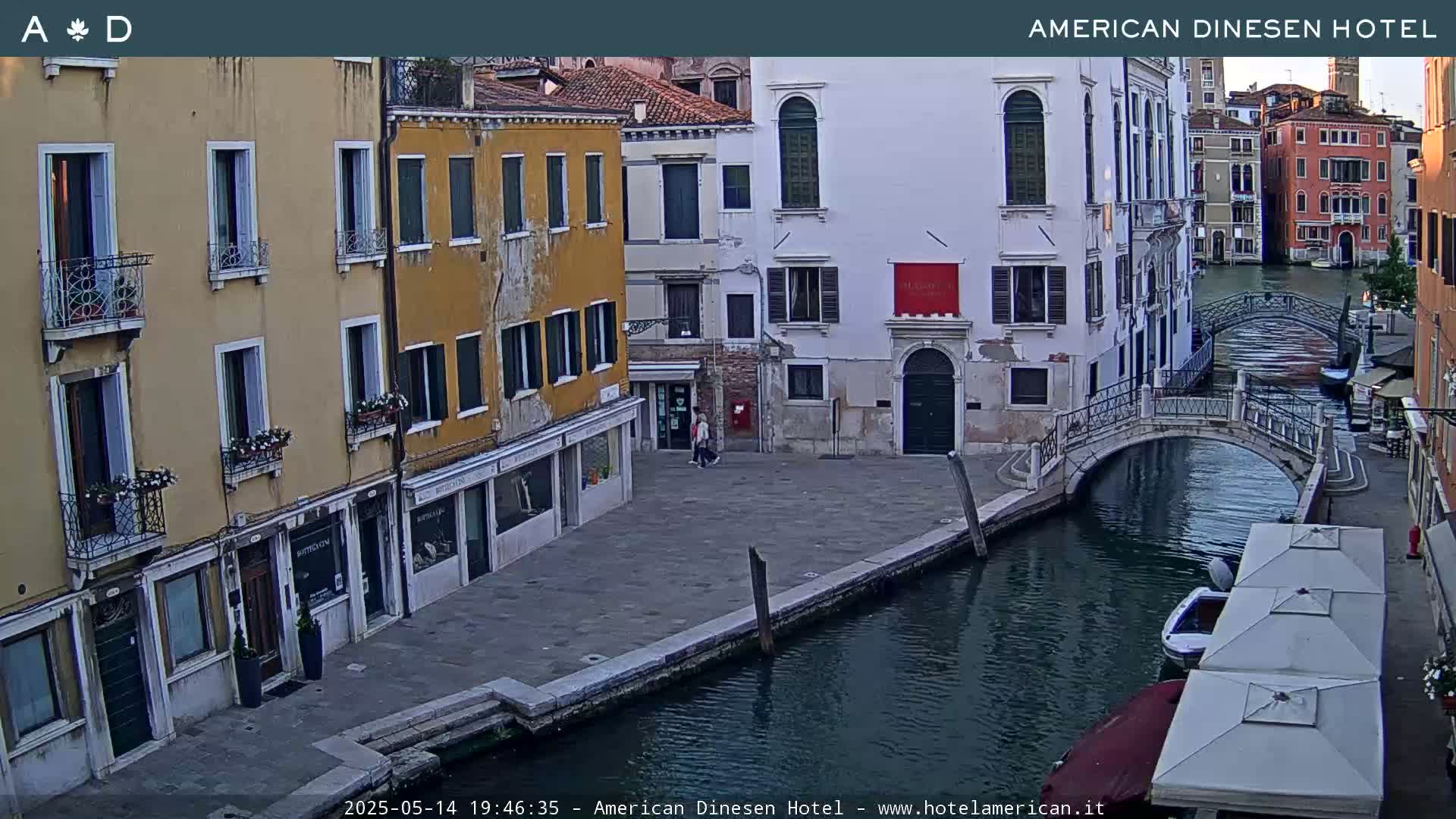A canal in Venice, Italy, shows several buildings lining its banks under a twilight sky, with a small bridge crossing the waterway and a few boats moored nearby.